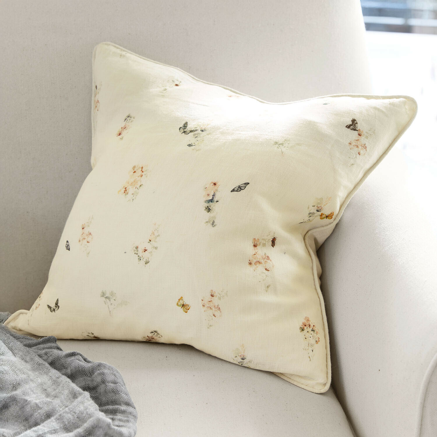Helles cremefarbenes Kissen mit zartem Blumen- und Schmetterlingsmuster auf Sofa, Wohnaccessoire