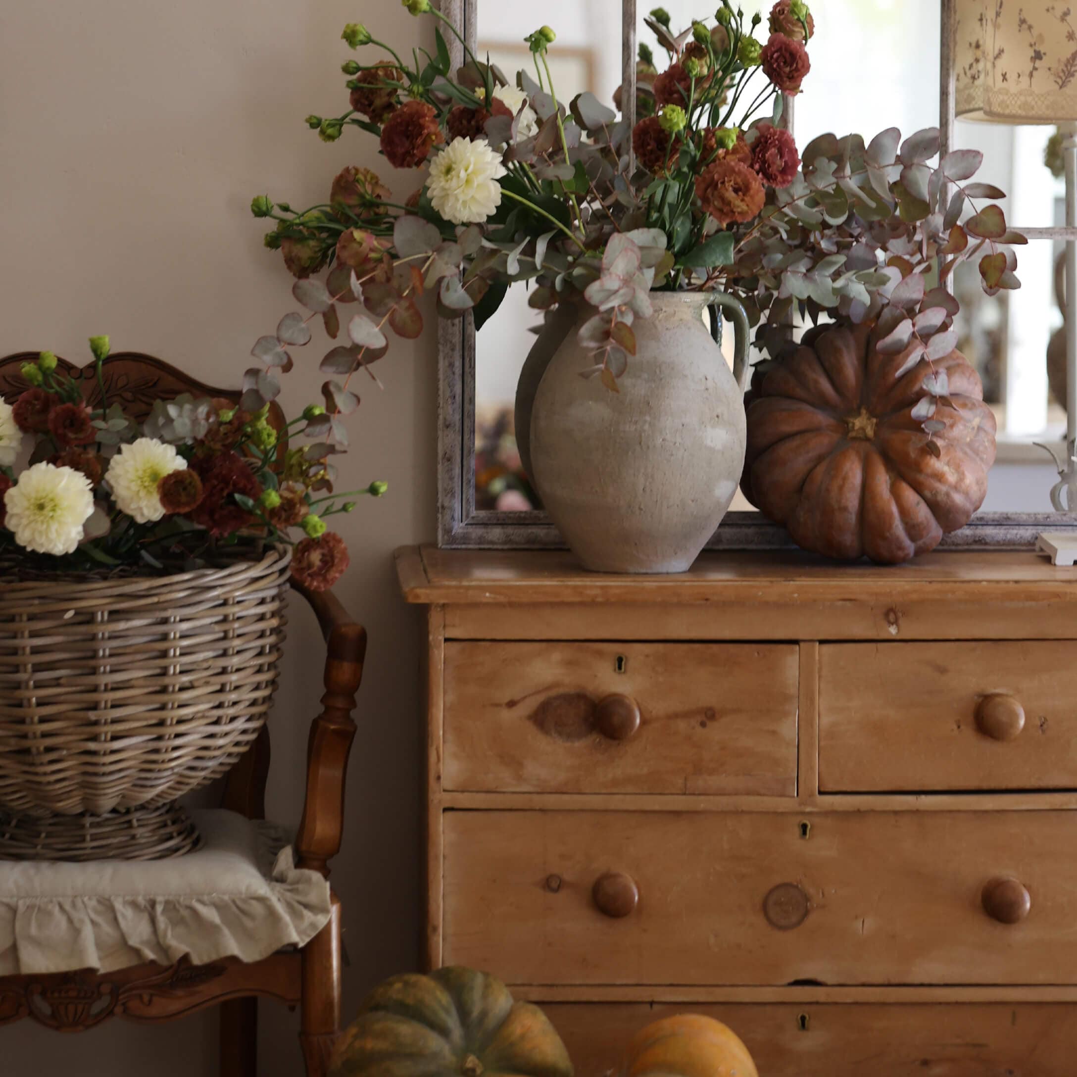 Rustikaler Holzkommode mit Tonvase, herbstlichem Blumenstrauß und dekorativen Kürbissen im gemütlichen Raum