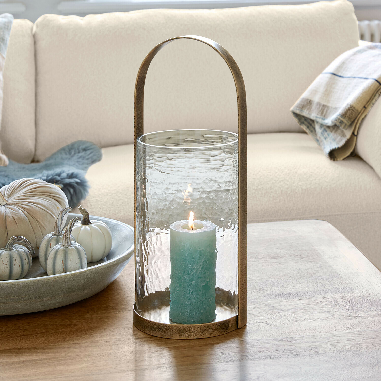 Glaslaterne mit Messinggriff und blauer Kerze auf Holztisch im Wohnzimmer
