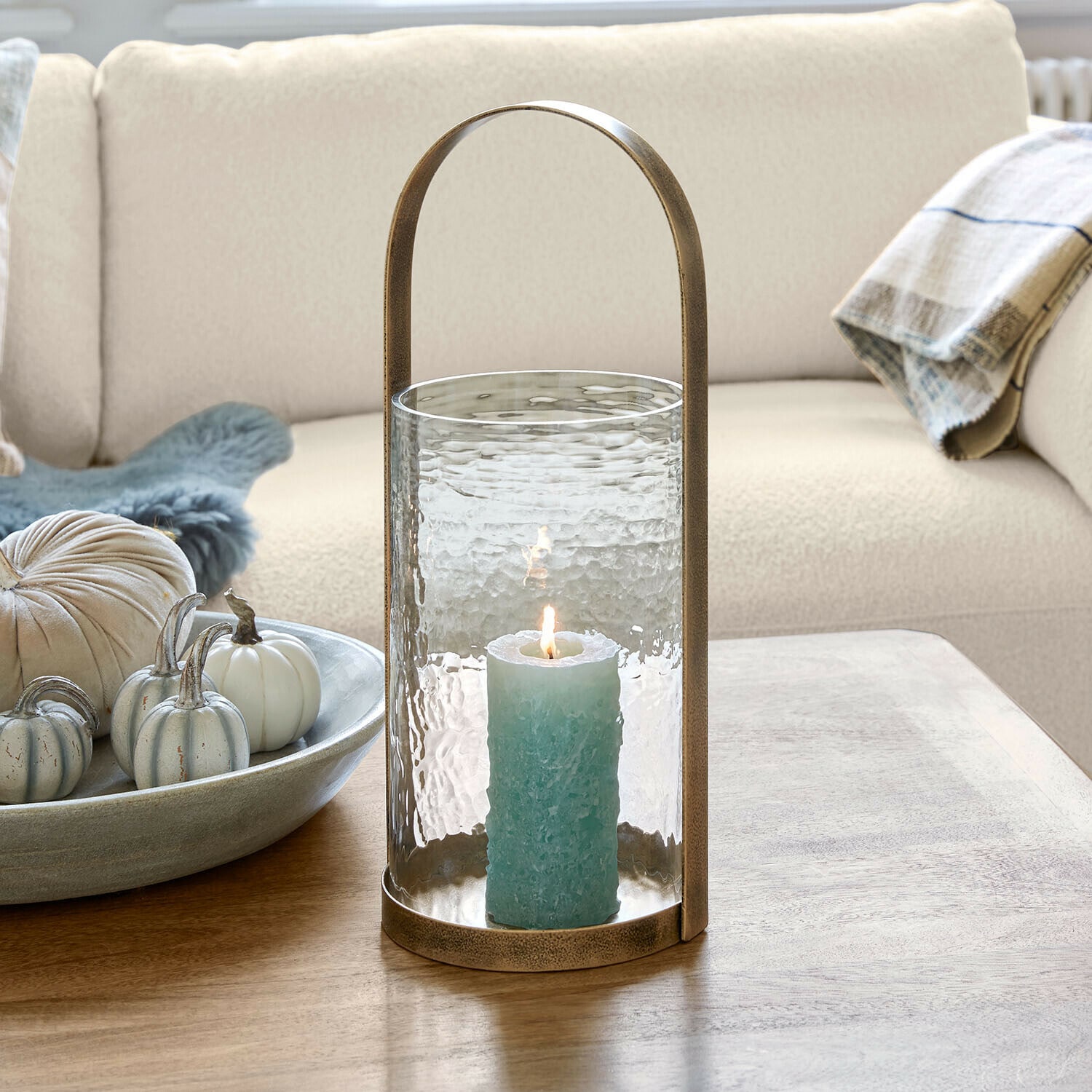 Windlicht Omirah Glaslaterne mit Messinggriff und blauer Kerze auf Holztisch im Wohnzimmer