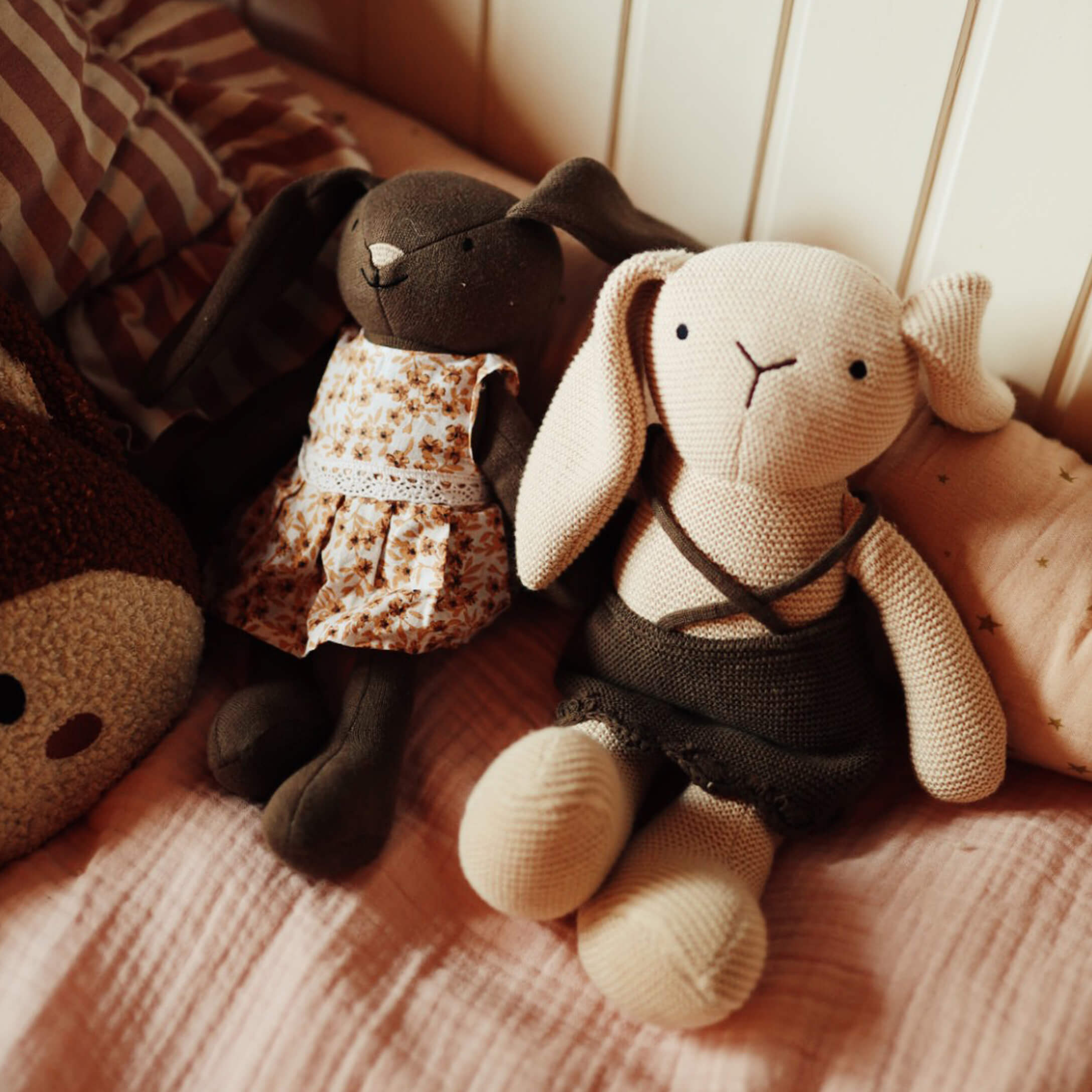 Zwei weiche Stoffhasen mit Kleidern auf rosa Bettdecke, Kinderzimmer Kuscheltiere