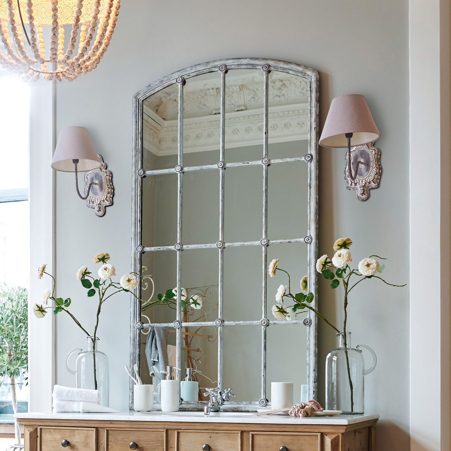 Spiegel Tobiah Großer Vintage-Spiegel mit Metallrahmen über Holzkommode mit Blumen und Wandlampen im Badezimmer