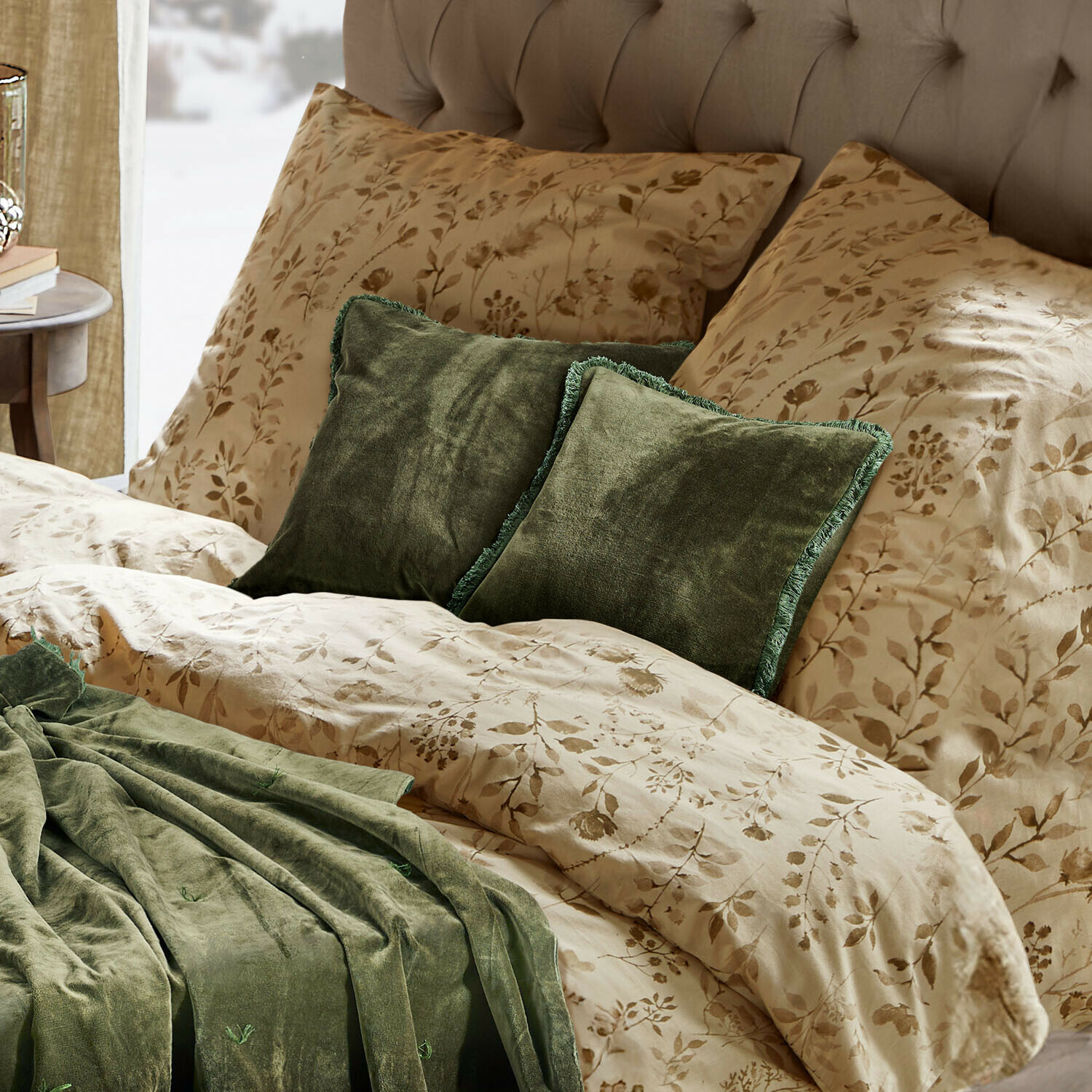 Beige Bettwäsche mit floralem Muster, grüne Samtkissen und Decke auf einem gepolsterten Bett