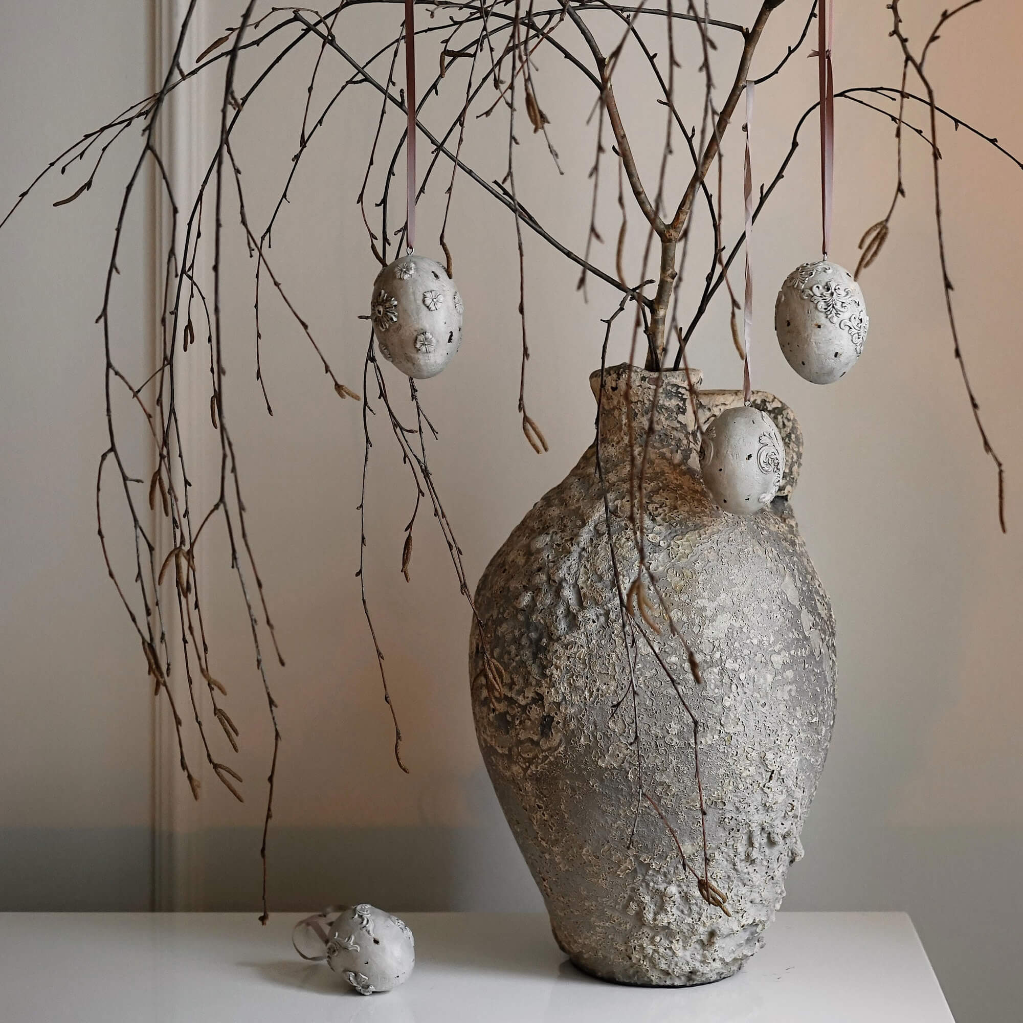 Rustikaler grauer Struktur-Vase mit Zweigen und dekorativen hängenden Ei-Anhängern