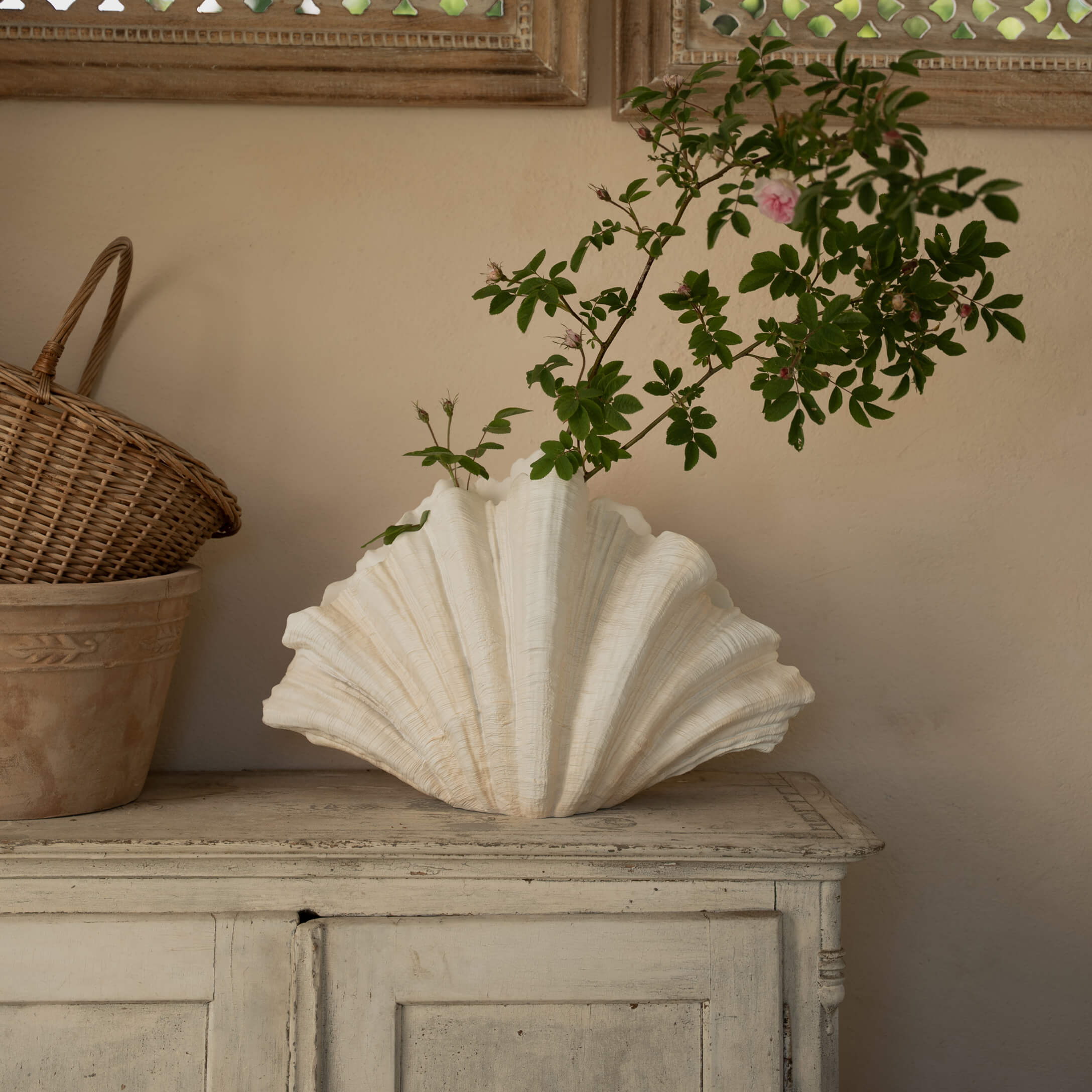 Weiße Keramikvase in Muschelform mit grünen Zweigen auf einem antiken Holzschrank