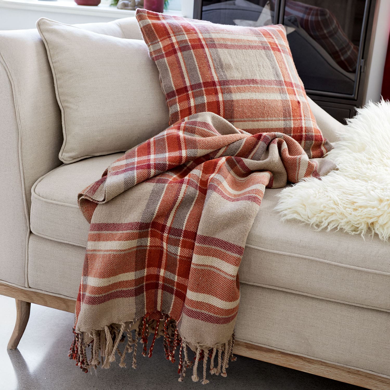 Beiges Sofa mit Kissen und kariertem Plaid in Rot- und Brauntönen für gemütliches Wohnzimmer