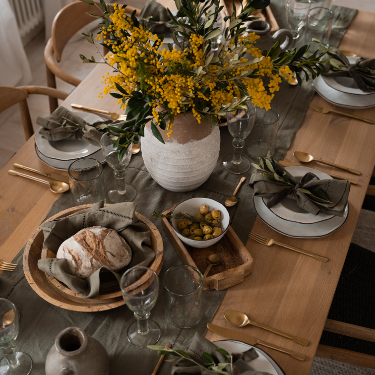 Rustikaler Holztisch mit weißen Keramiktellern, Holzschalen und gelben Blumen in Tonvase