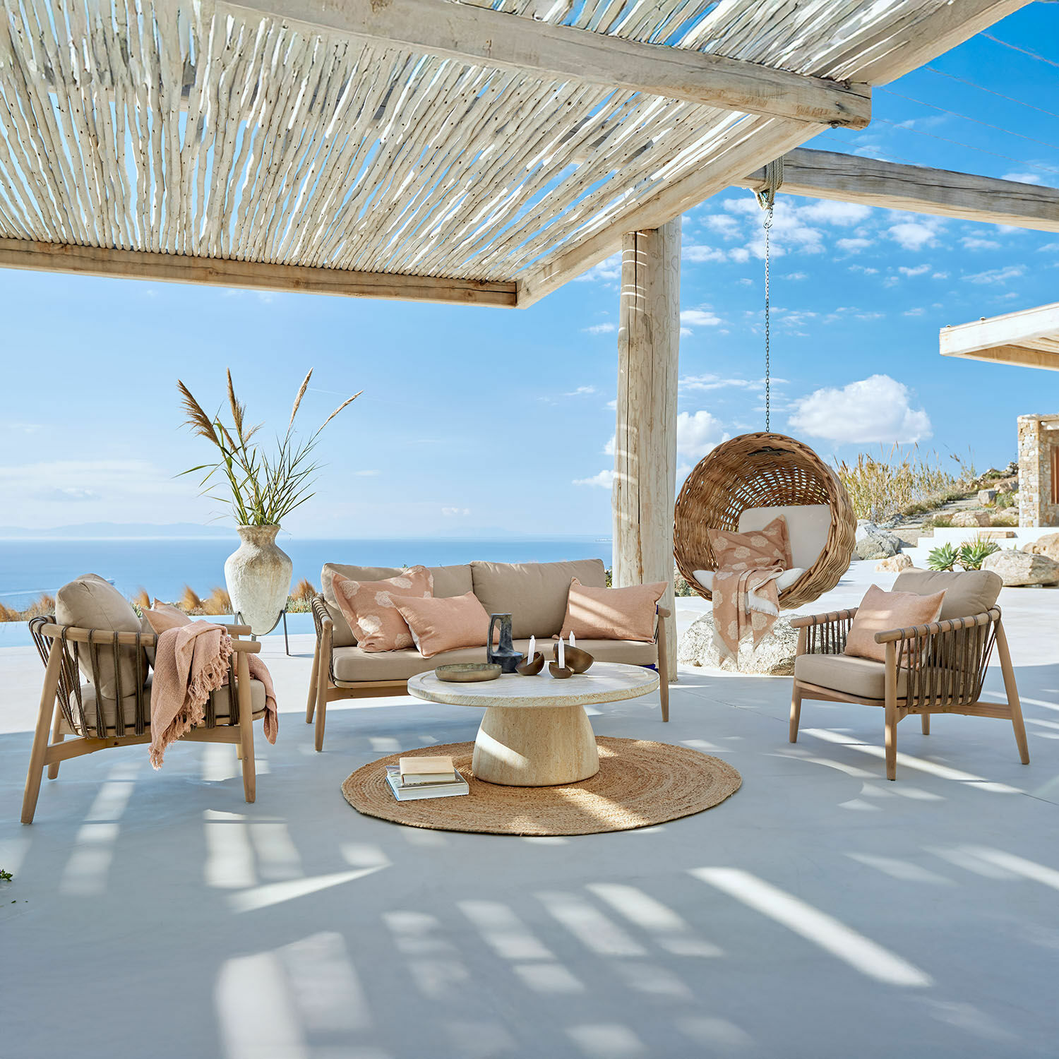 Sitzgruppe FSC®-100% Thornwick Outdoor-Möbelset mit beigen Polstern und hängendem Korbsessel auf Terrasse mit Meerblick