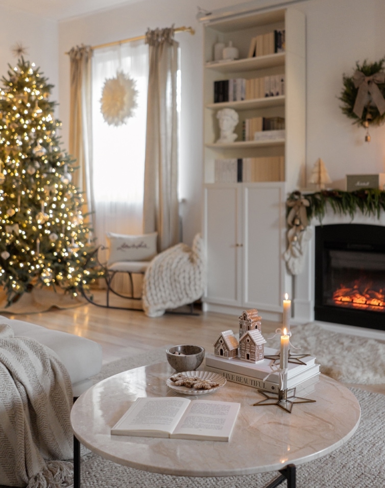 Gemütliches Wohnzimmer mit hellem Marmortisch, beleuchtetem Weihnachtsbaum und brennendem Kamin