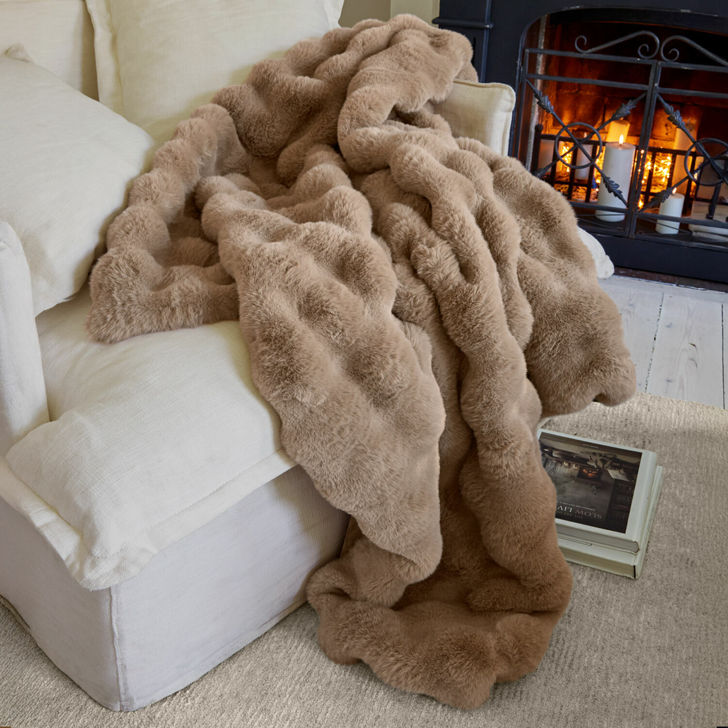Plaid Zalina Weiche beige Kunstfell-Decke auf hellem Sofa vor Kamin für gemütliche Wohnatmosphäre