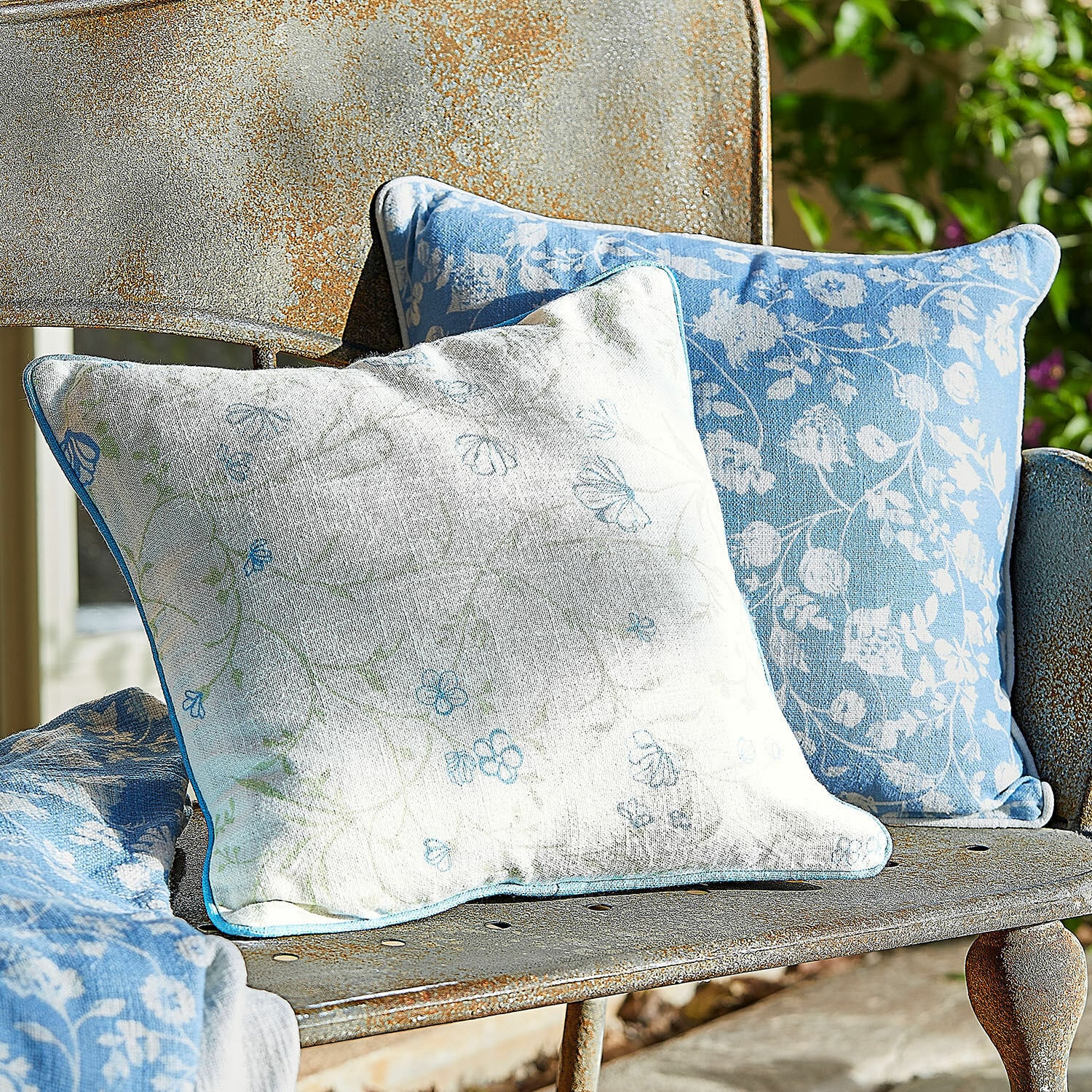 Kissenhülle 2er Set Corvelique Zwei dekorative Baumwollkissen in Blau-Weiß mit Blumenmuster auf rostiger Metallbank im Garten