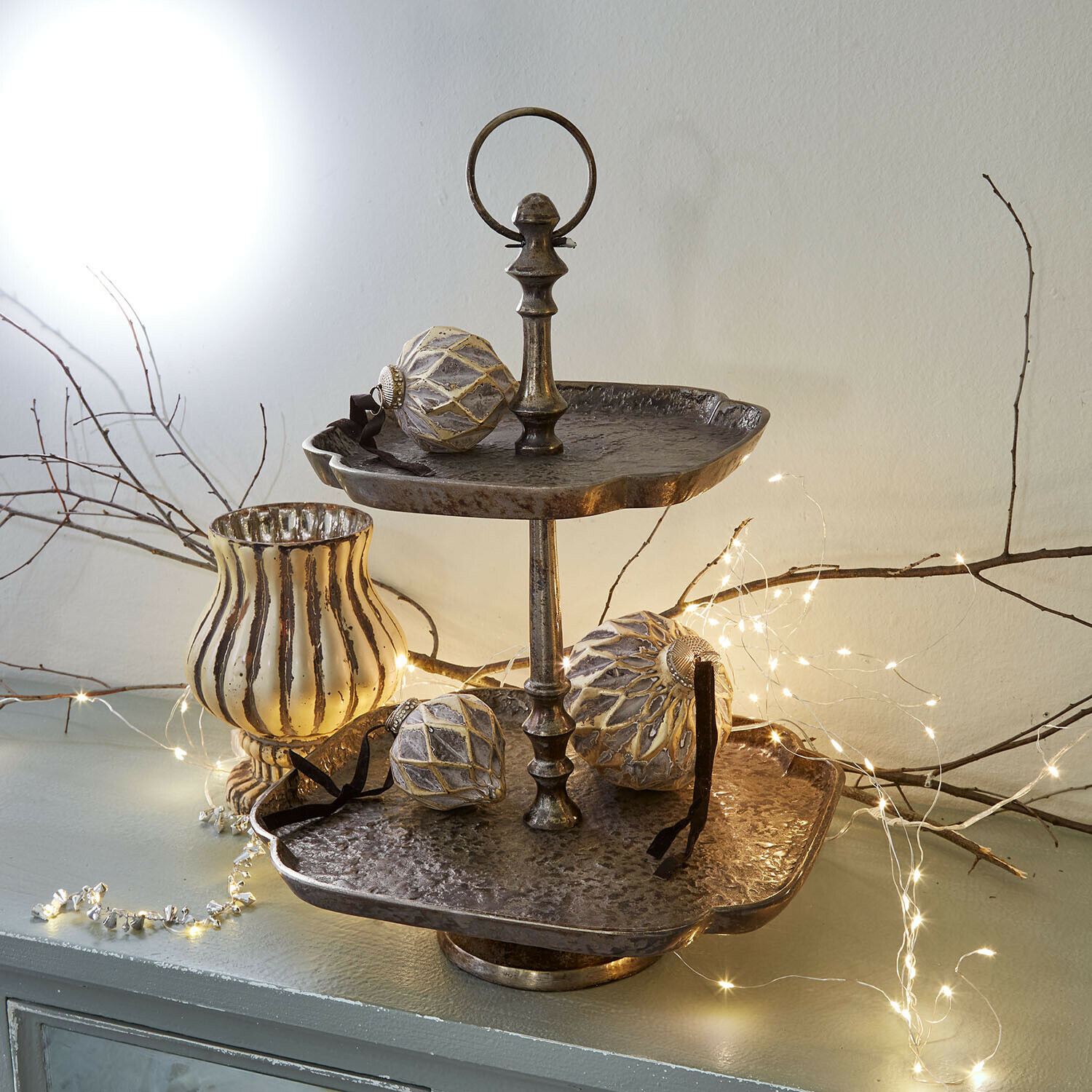 Etagere Lazmina Zweistöckige Metall-Etagere im Vintage-Stil mit Weihnachtskugeln und LED-Lichterkette dekoriert