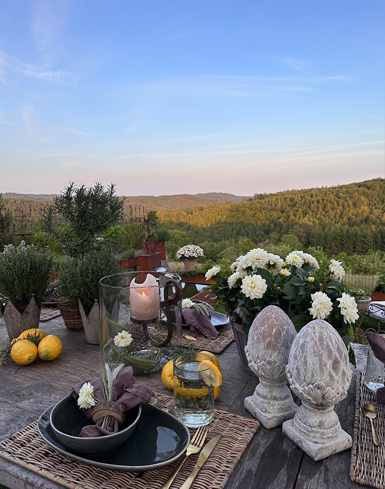 Rustikaler Tisch mit Steindekorationen und weißen Blumen vor grünen Hügeln und blauem Himmel