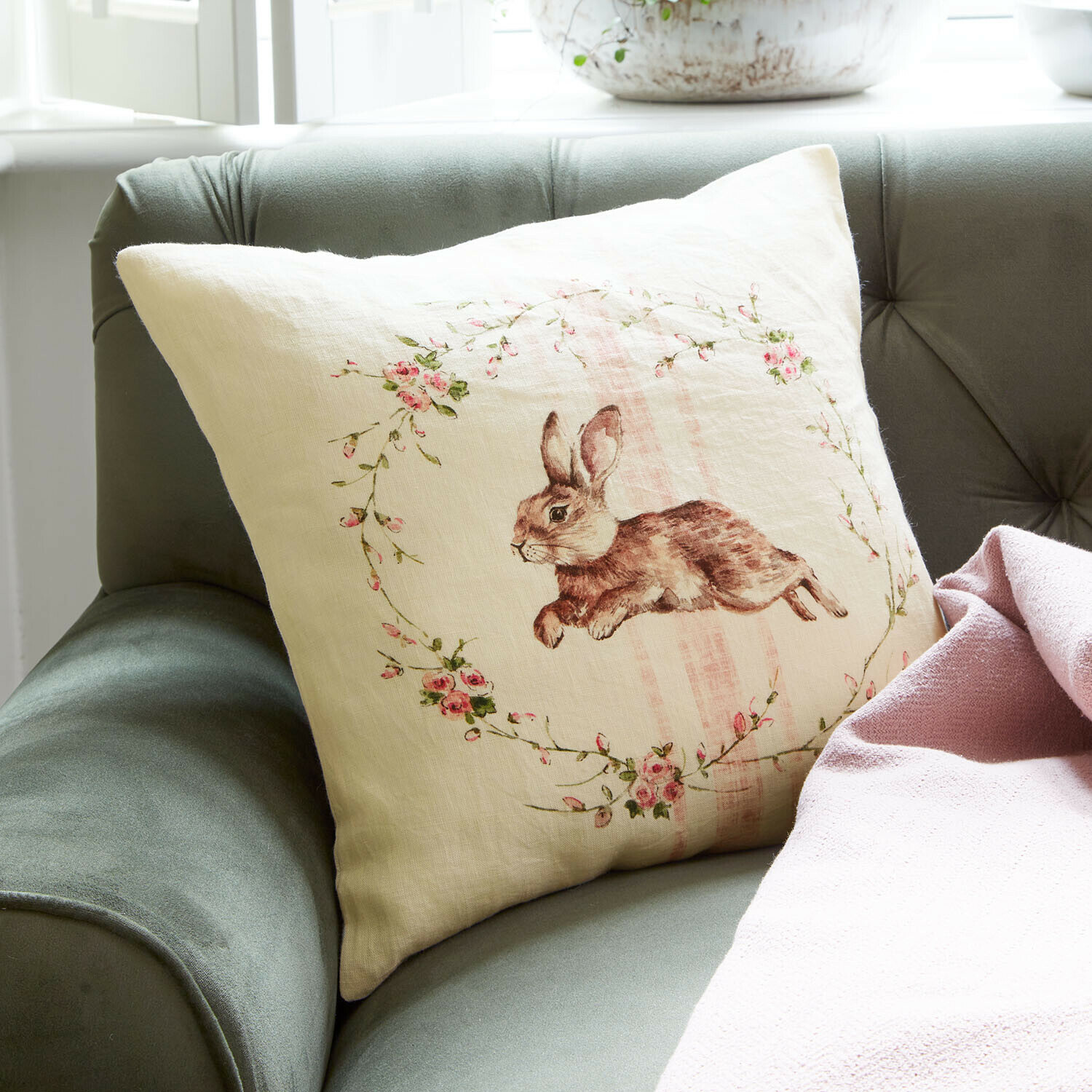 Kissenhülle Ravencrest Beige Leinenkissen mit Hasenmotiv und rosa Blumen auf grünem Sofa mit rosa Decke