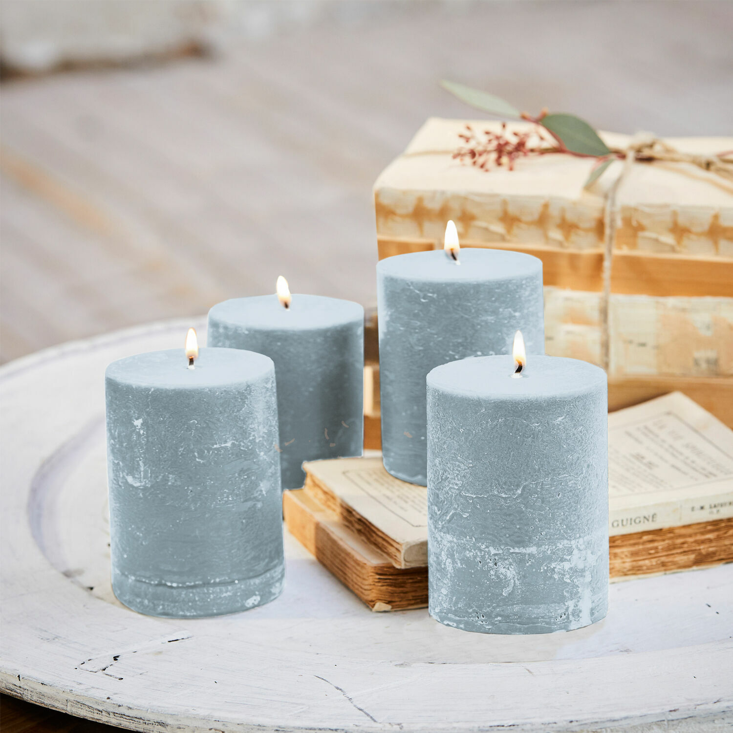 Kerze 4er Set Virrans Set aus vier blauen Wachskerzen auf weißem Holztisch mit Büchern und Geschenkbox