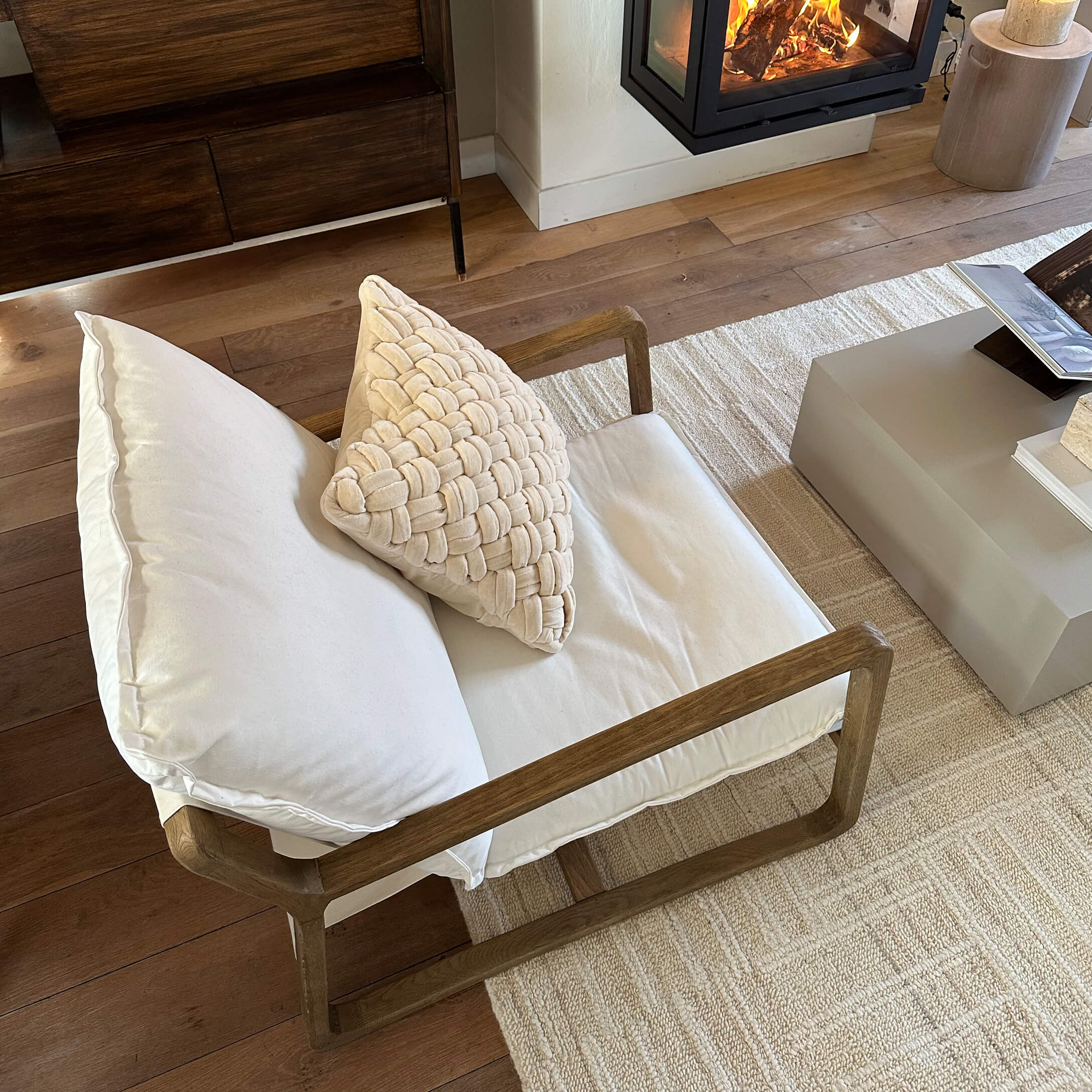 Sessel mit Holzrahmen und cremefarbenen Kissen auf hellem Teppich neben Kamin im Wohnzimmer