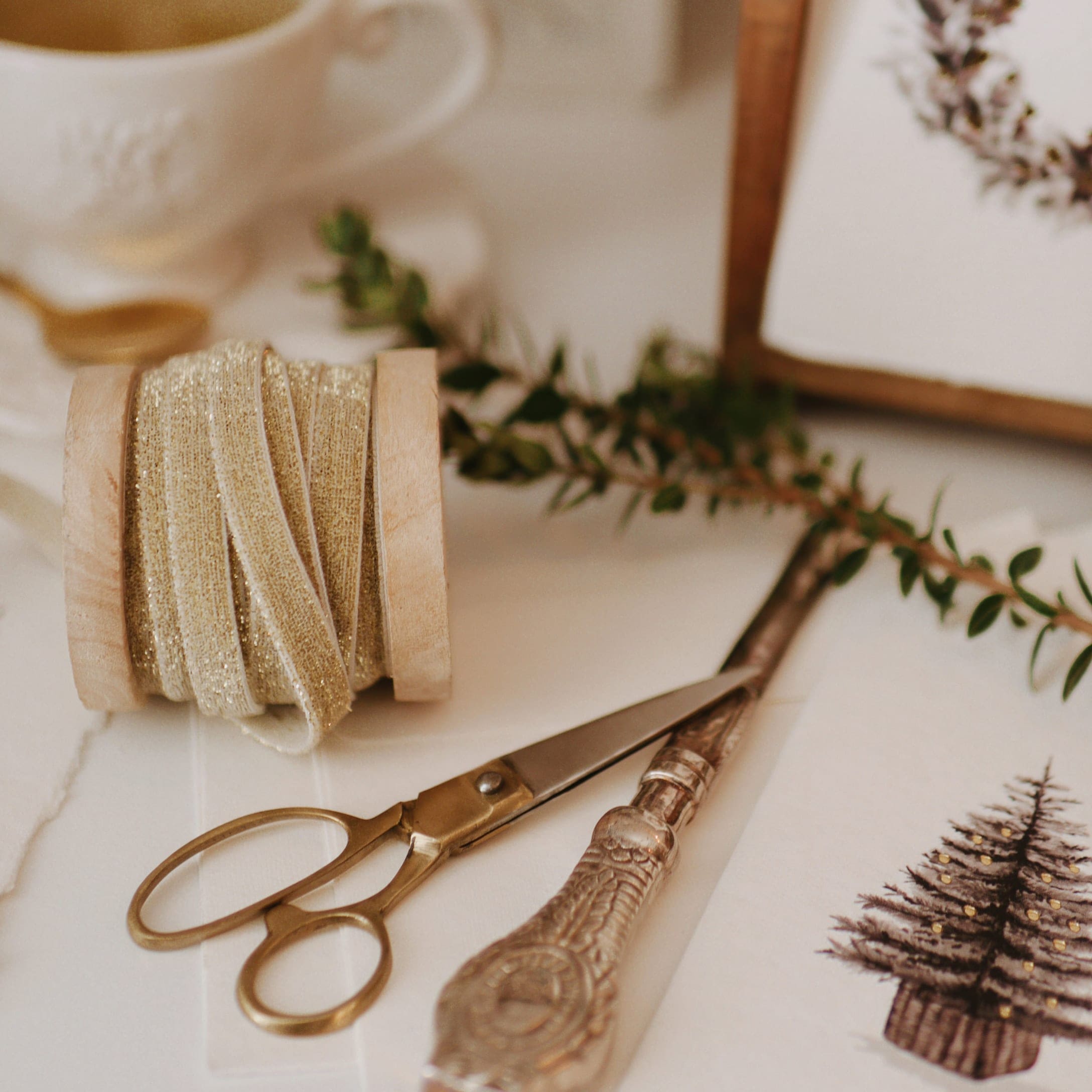 Goldglänzendes Glitzerband auf Holzspule mit Schere und Weihnachtskarte mit Tannenbaum