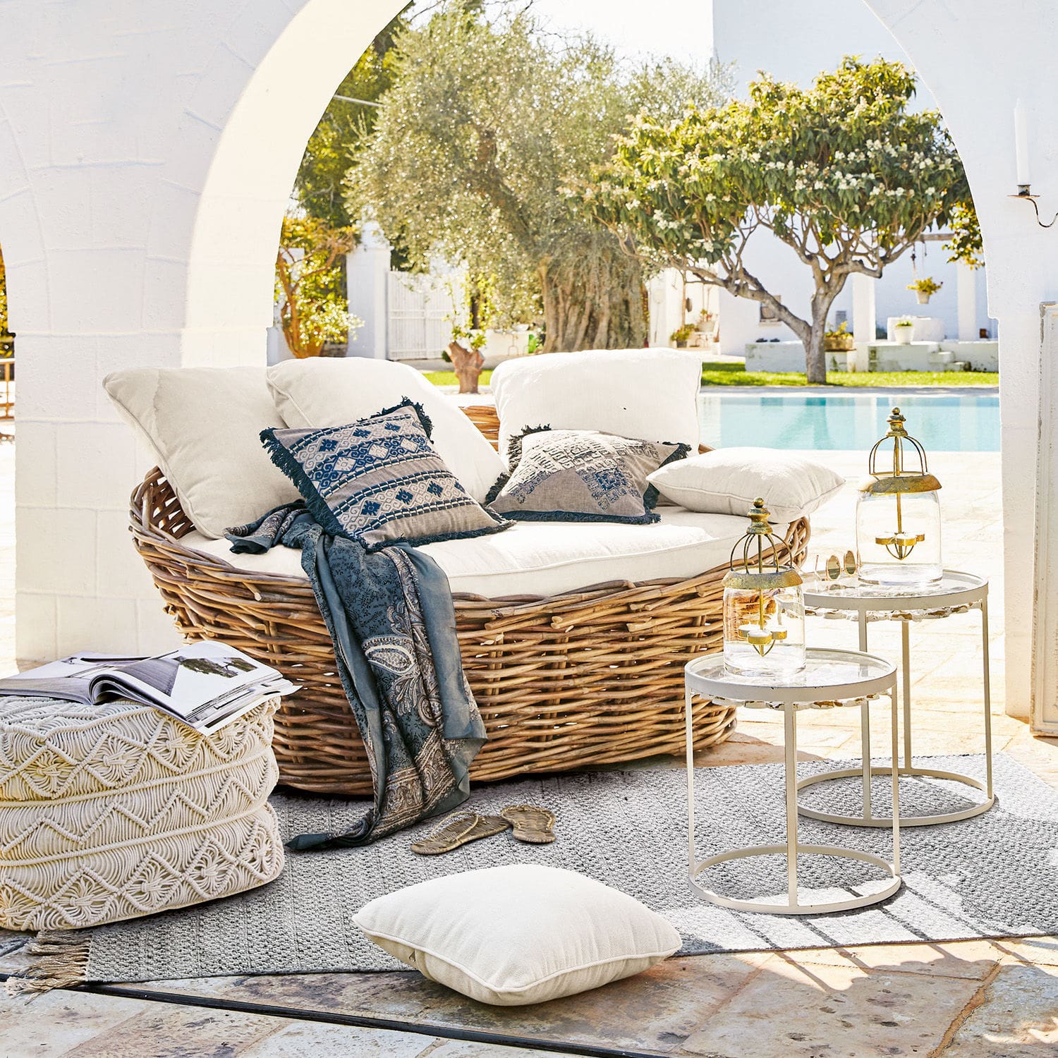 Rundes Rattan-Sofa mit cremefarbenen Kissen und blauem Plaid am Pool im Boho-Stil