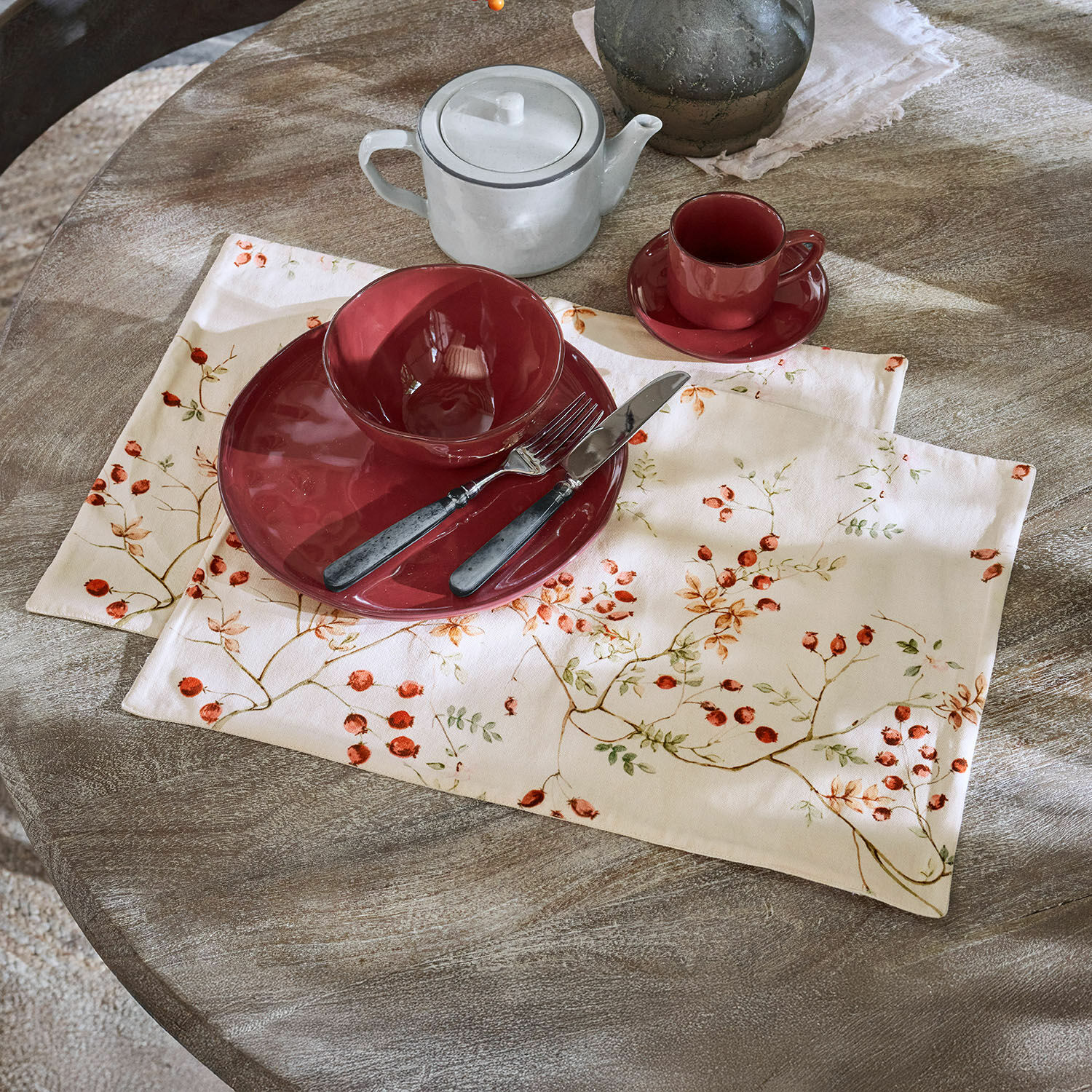 Rotes Keramikgeschirr auf Leinentischset mit Fruchtmotiv auf rustikalem Holztisch