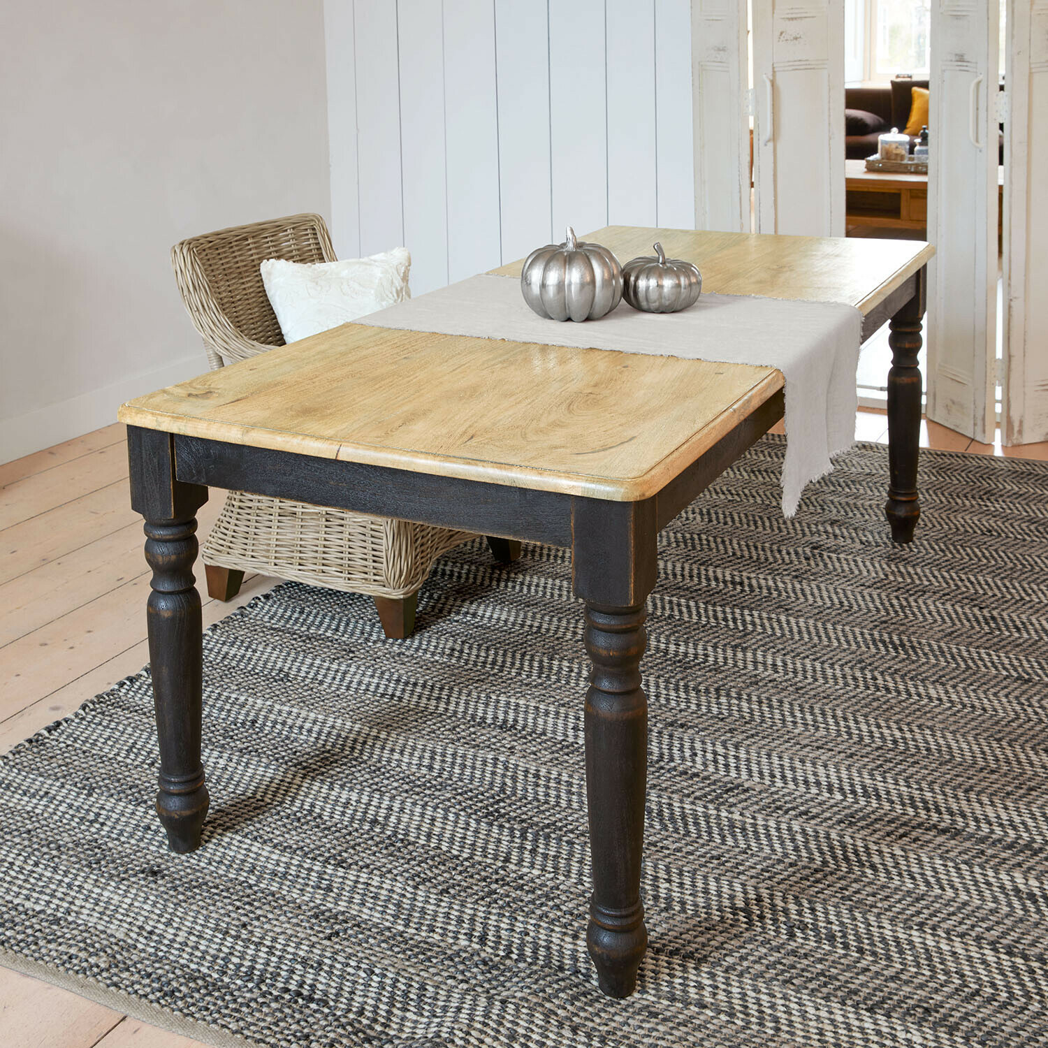 Tisch Mont Lisan Holztisch mit hellem Holzplatte und schwarzen Beinen auf grauem Teppich mit silbernen Metallkürbissen