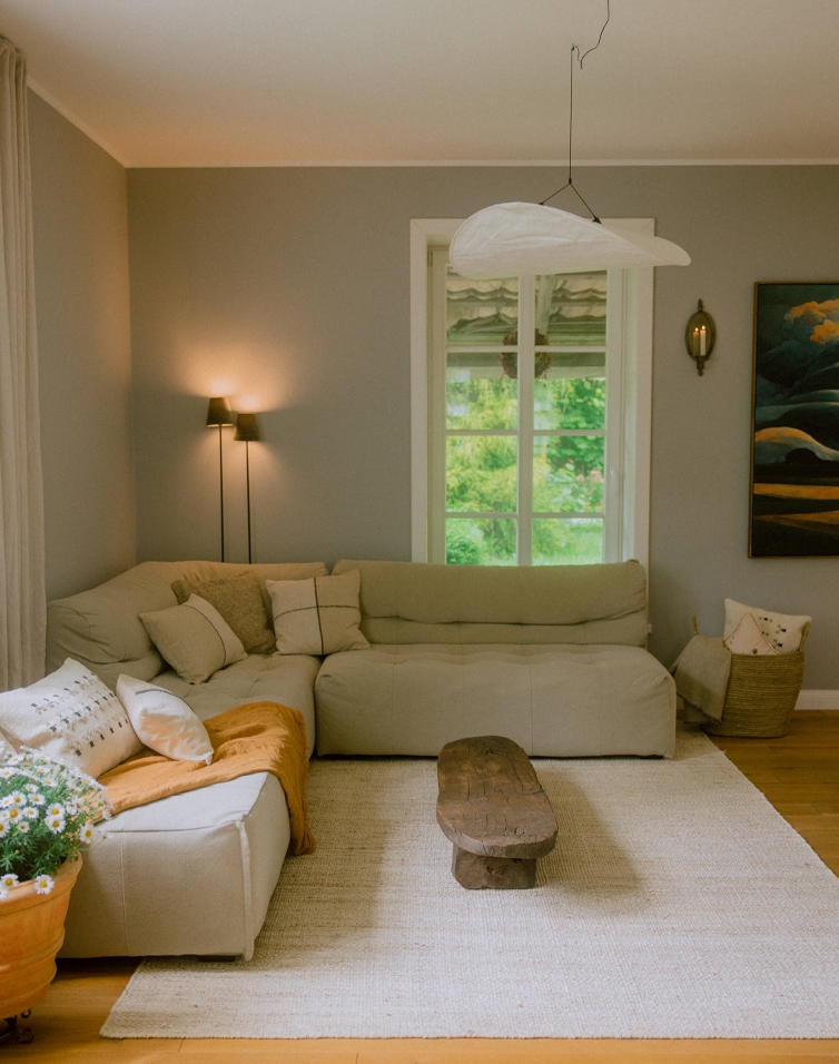 Gemütliches Wohnzimmer mit beigem Ecksofa, rustikalem Holztisch und hellem Teppich im skandinavischen Stil