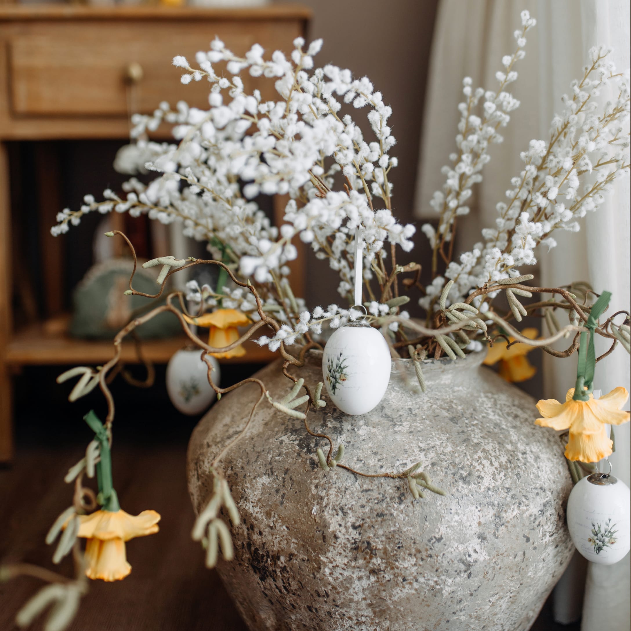 Großer grauer Keramikvase mit weißen Zweigen und gelben Blumen als Frühlingsdeko im Raum