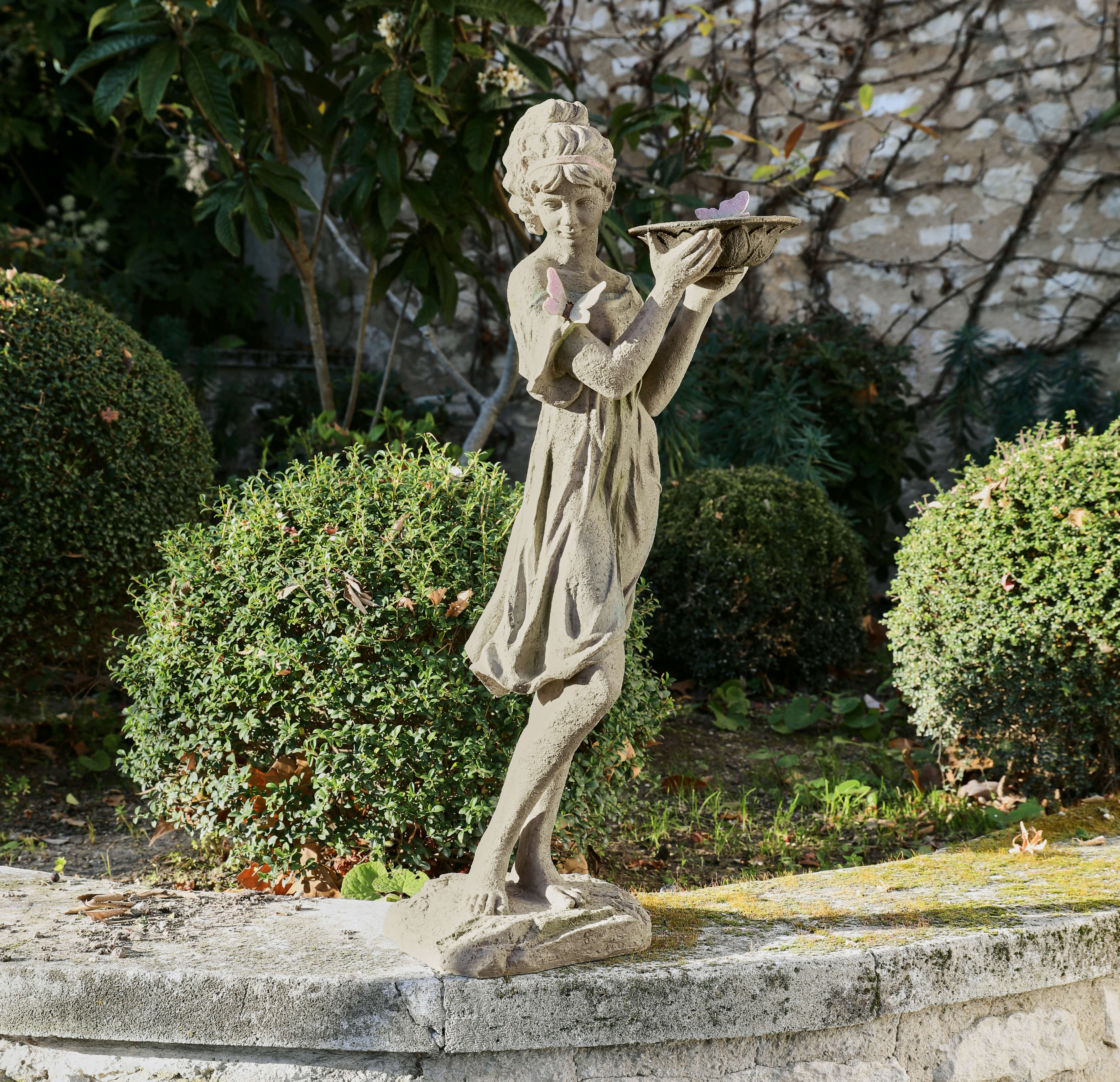 Gartenfigur aus Beton einer Mädchenstatue mit Schmetterlingen, dekorativ im grünen Garten platziert