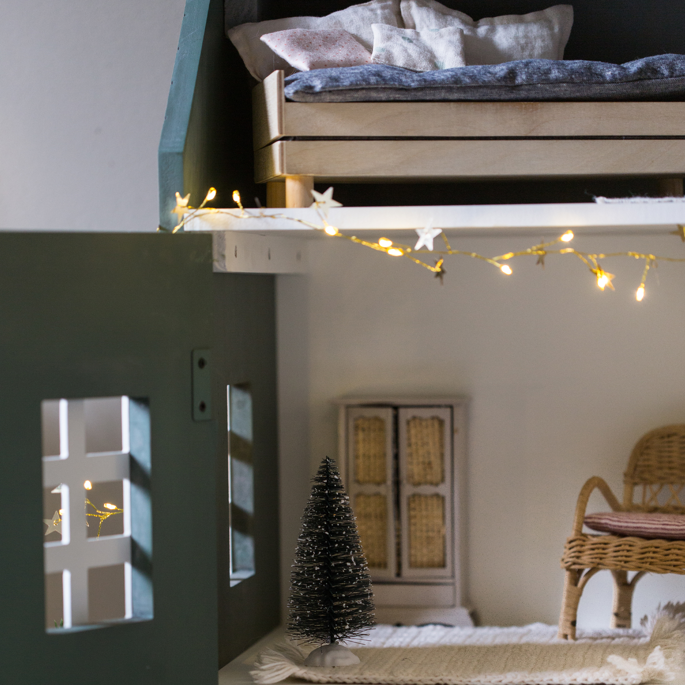 Kleiner schwarzer Deko-Tannenbaum aus Fasern auf weißem Teppich in gemütlichem Kinderzimmer mit Lichterkette