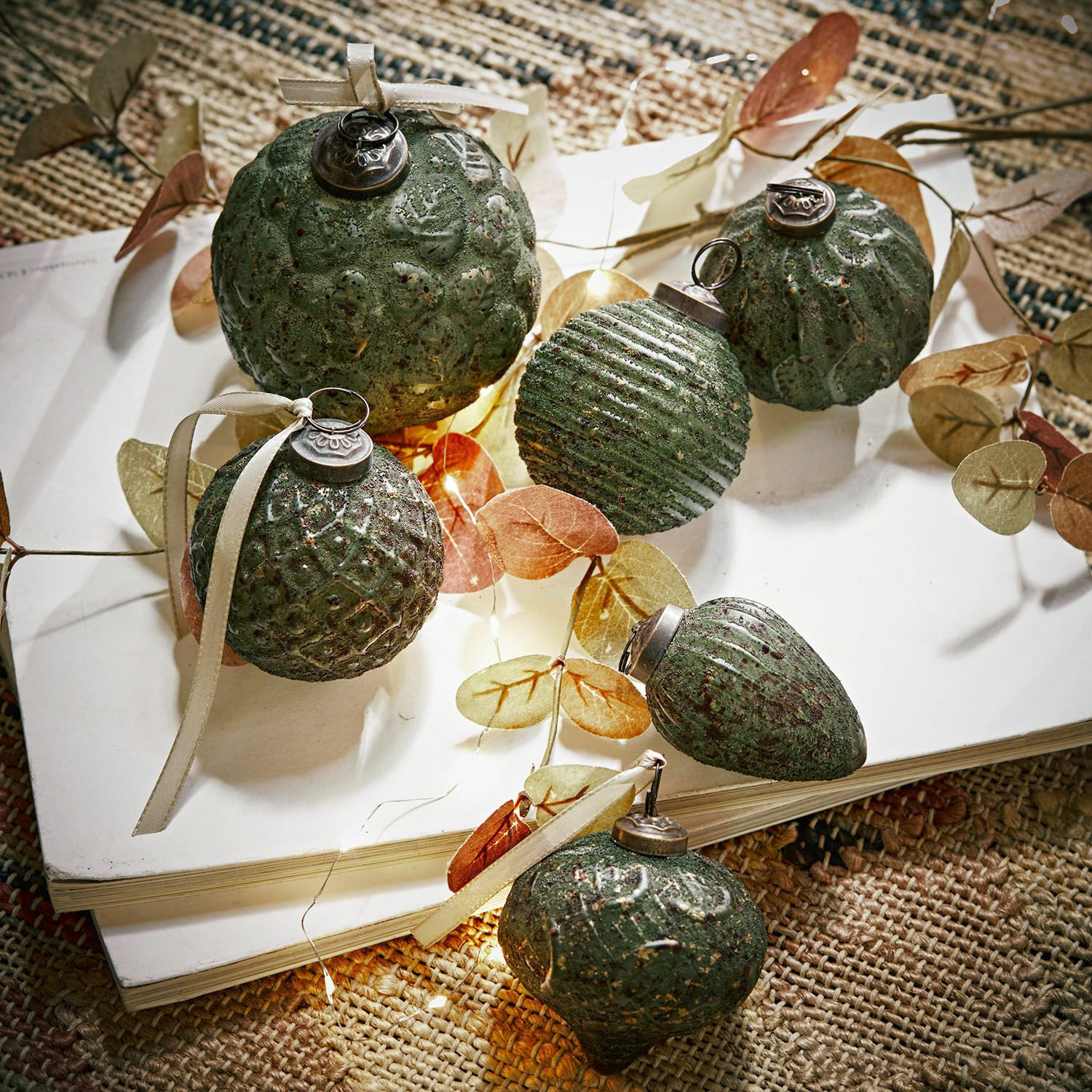 Weihnachtsschmuck 6er Set Moriches Set aus grünen, strukturierten Weihnachtskugeln mit Bändern auf weißem Buch auf Naturteppich
