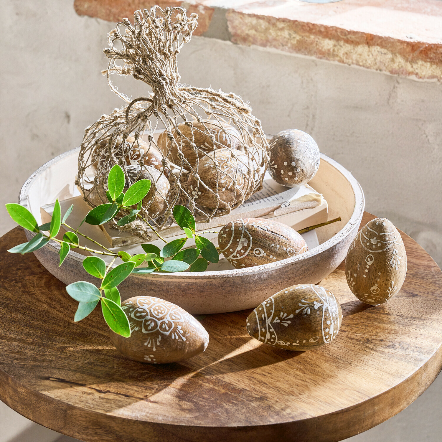 Holzeier mit weißem Muster in Schale auf Holztisch mit grünen Blättern als Dekoration