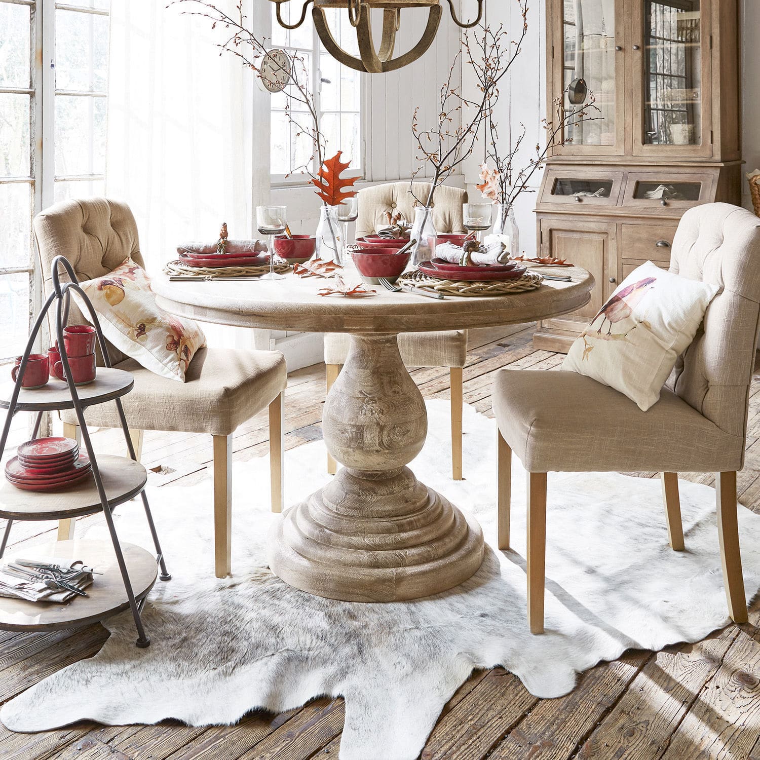 Tisch Orlin Heller runder Holztisch mit beigen Polsterstühlen und roten Accessoires in gemütlichem Esszimmer