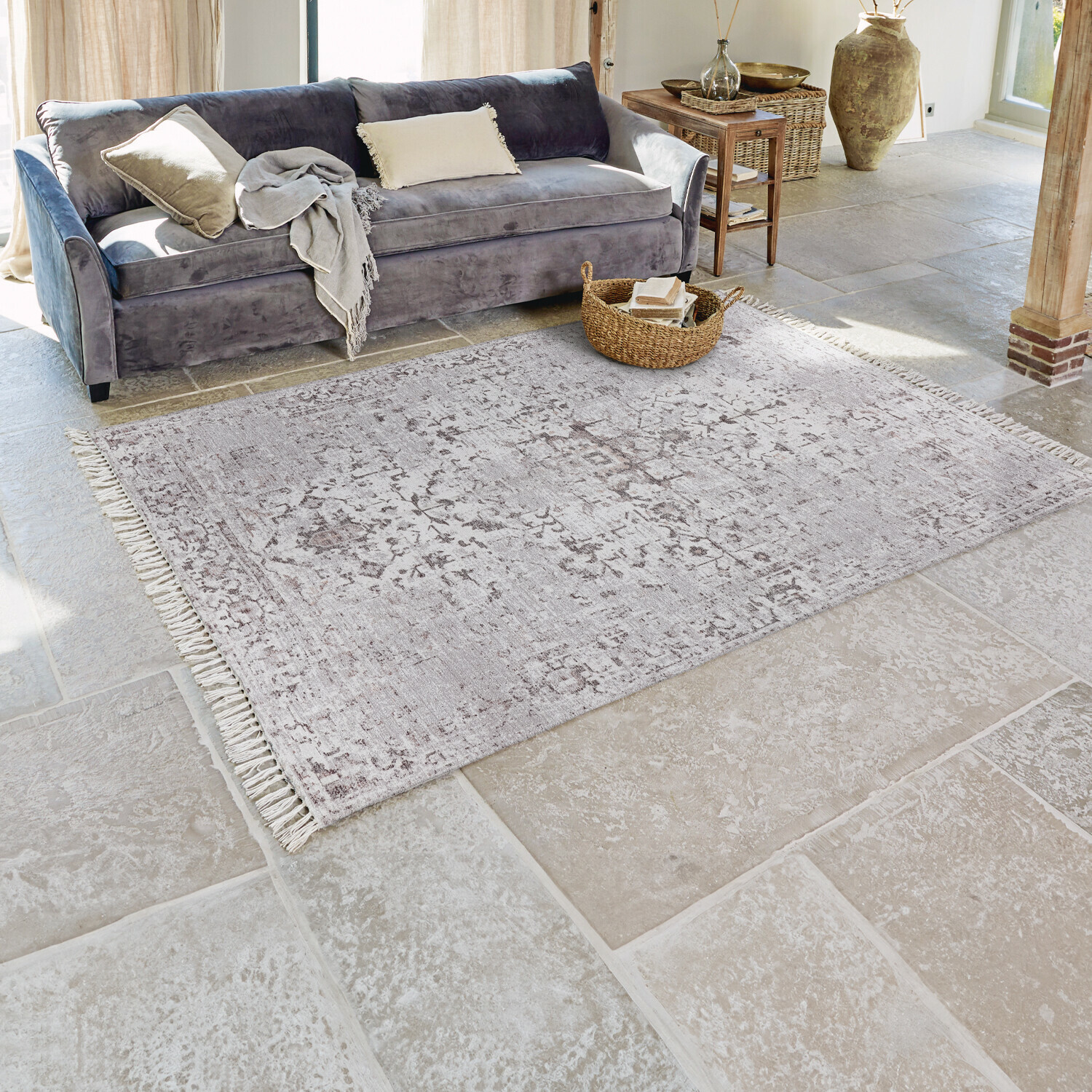 Grauer Teppich mit feinem Muster und Fransen auf hellem Steinboden im Wohnzimmer mit grauem Sofa