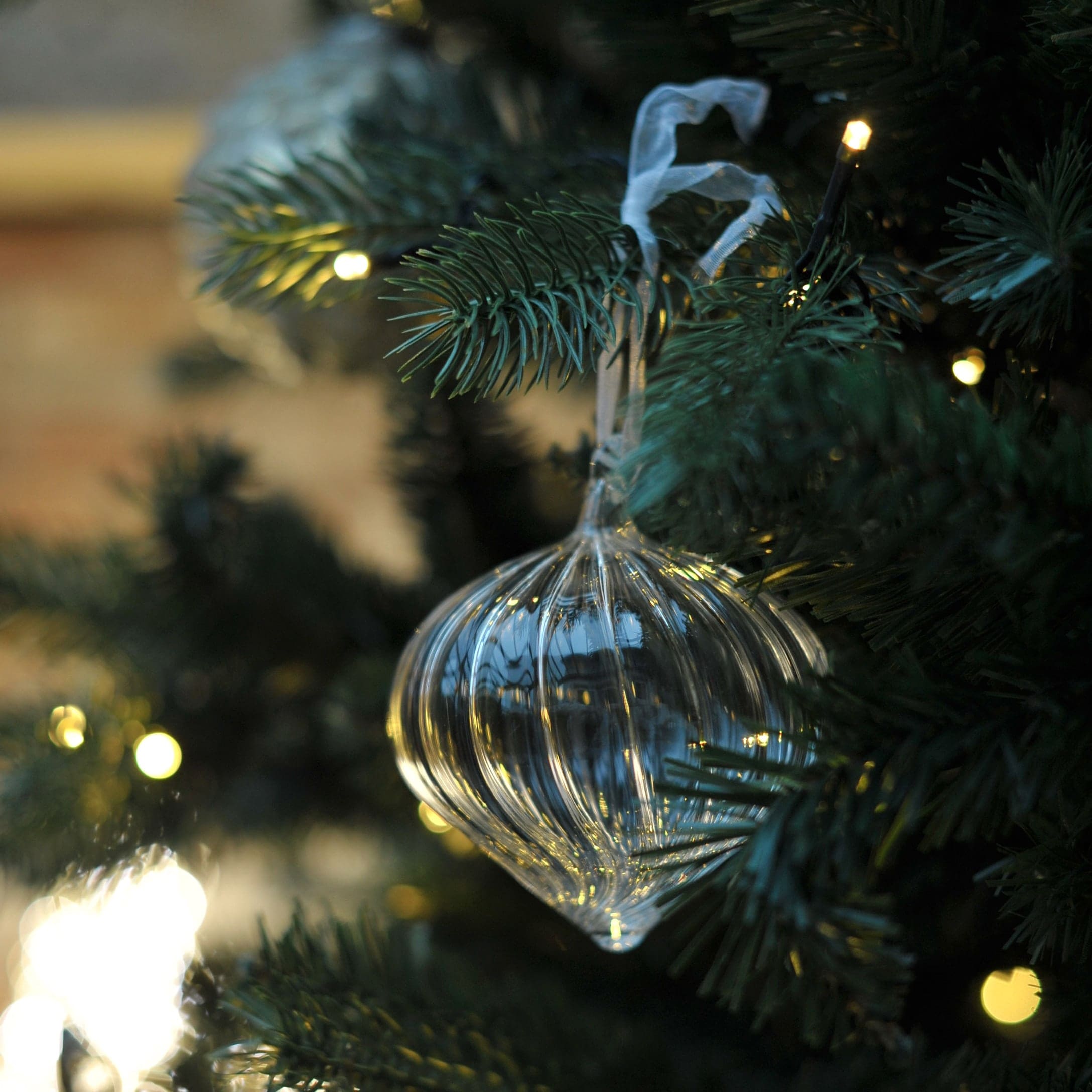 Transparanter Glas-Weihnachtsschmuck in Zwiebel-Form an grüner Tannenzweig mit Lichterkette