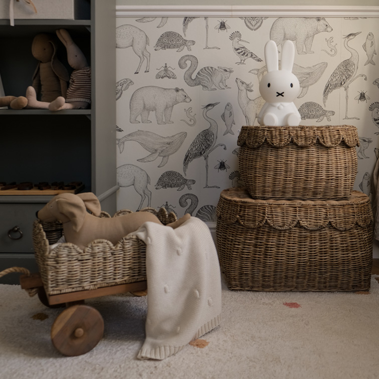 Zwei braune Rattankörbe mit Hasenlampe und Spielzeug in einem Kinderzimmer mit Tiermuster-Tapete