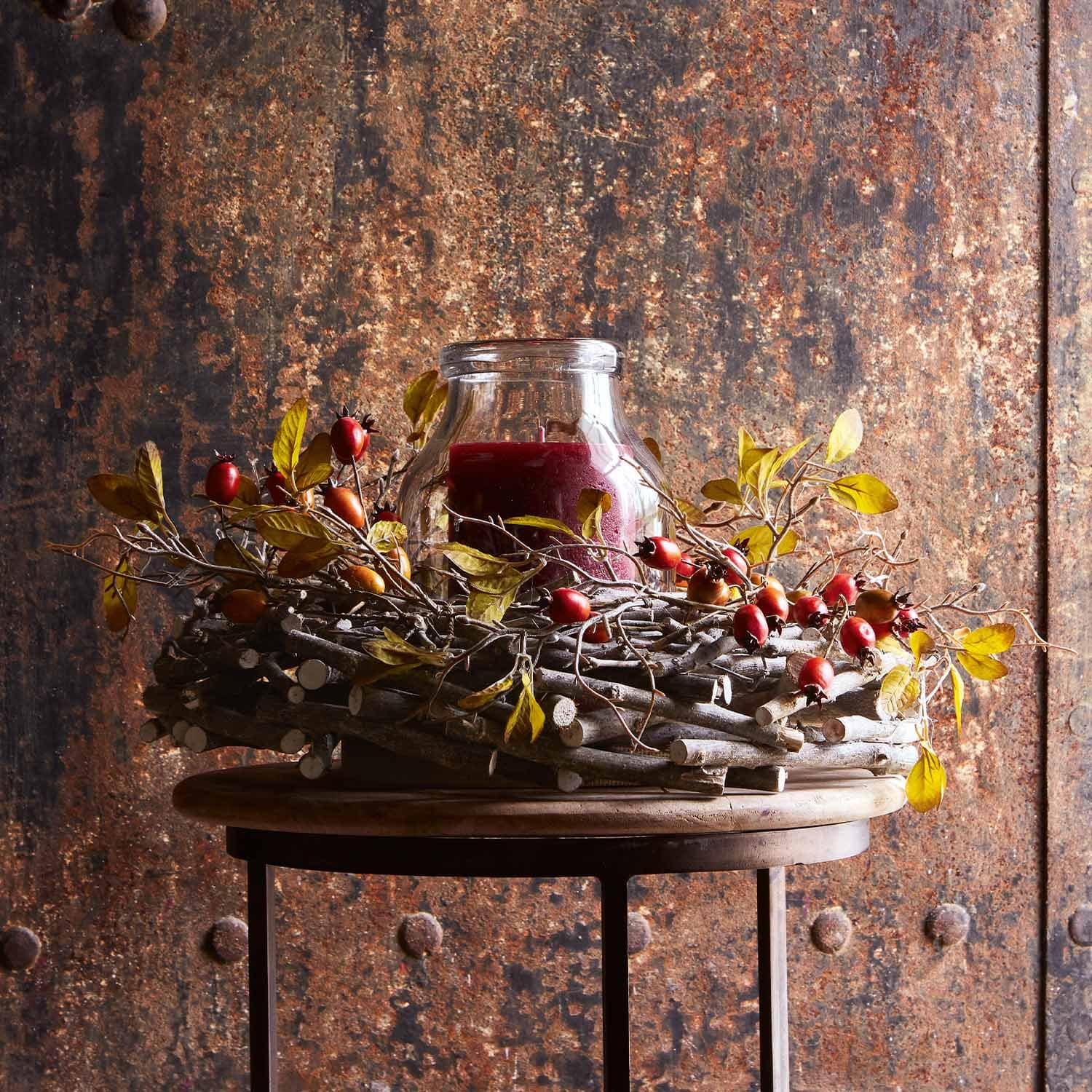 Dekorativer Kranz aus Zweigen mit roten Beeren und roter Glas-Kerze auf Holztisch