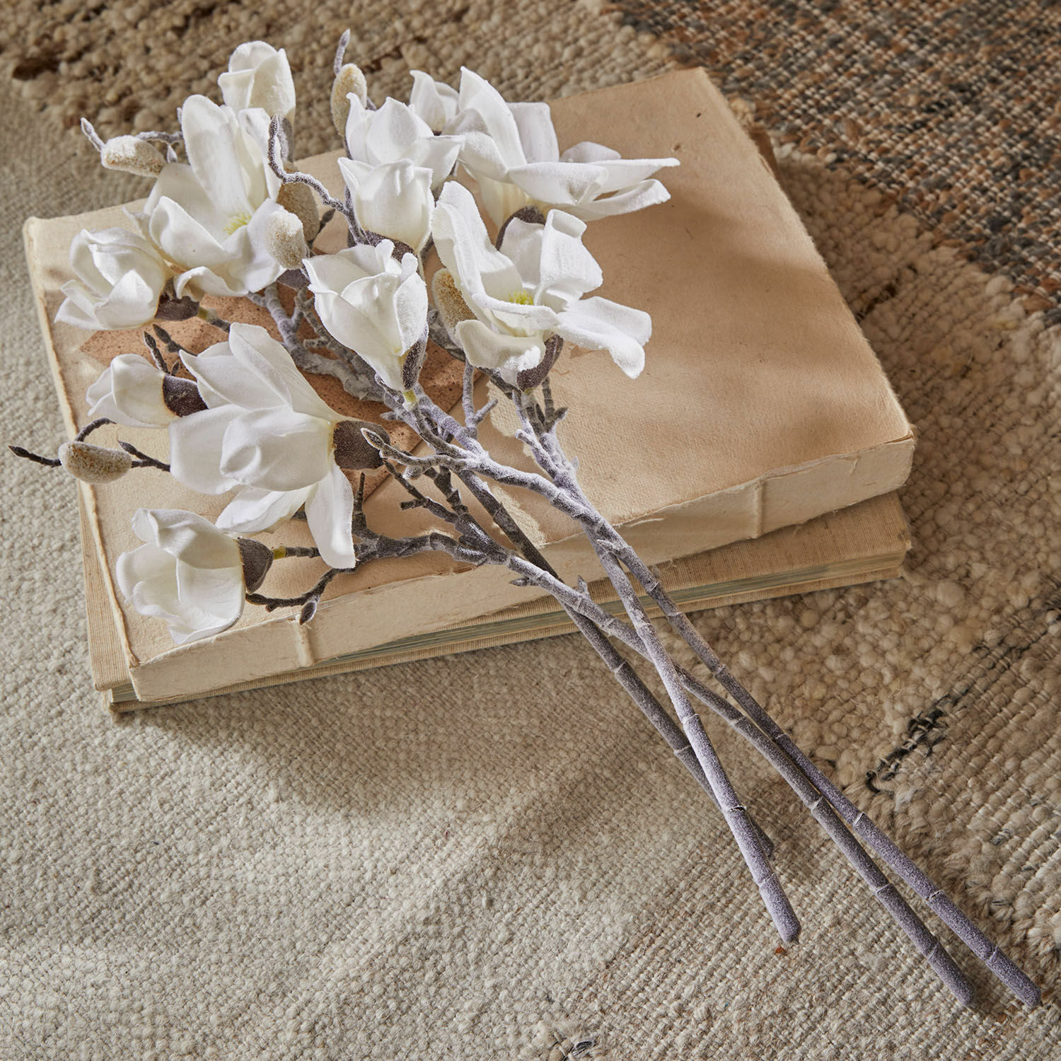 Deko-Blume 4er Set Santavella Strauß aus weißen Magnolienblüten aus Stoff auf beigen Büchern auf strukturiertem Teppich