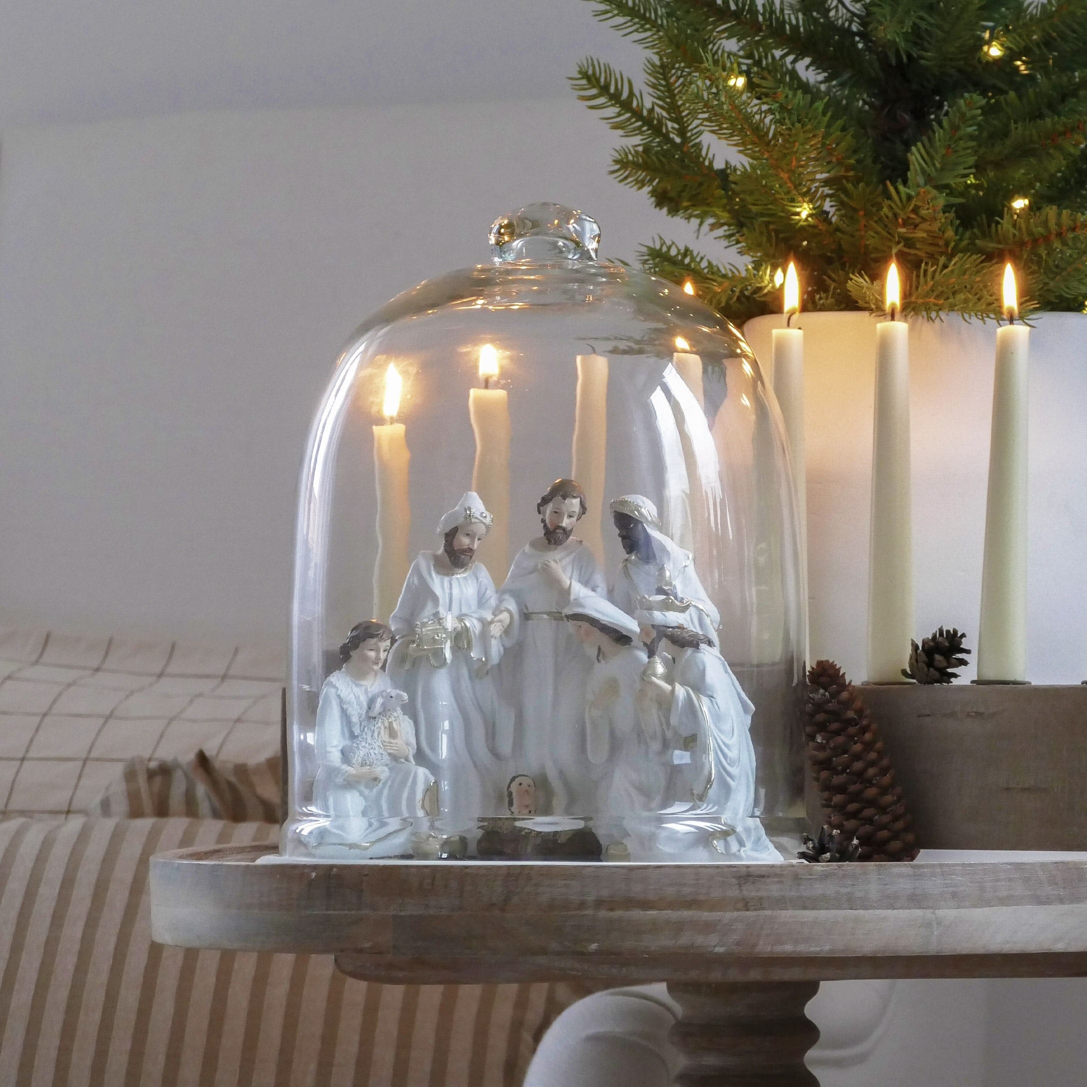 Weiße Keramik-Krippe unter Glashaube mit brennenden Kerzen und weihnachtlicher Dekoration