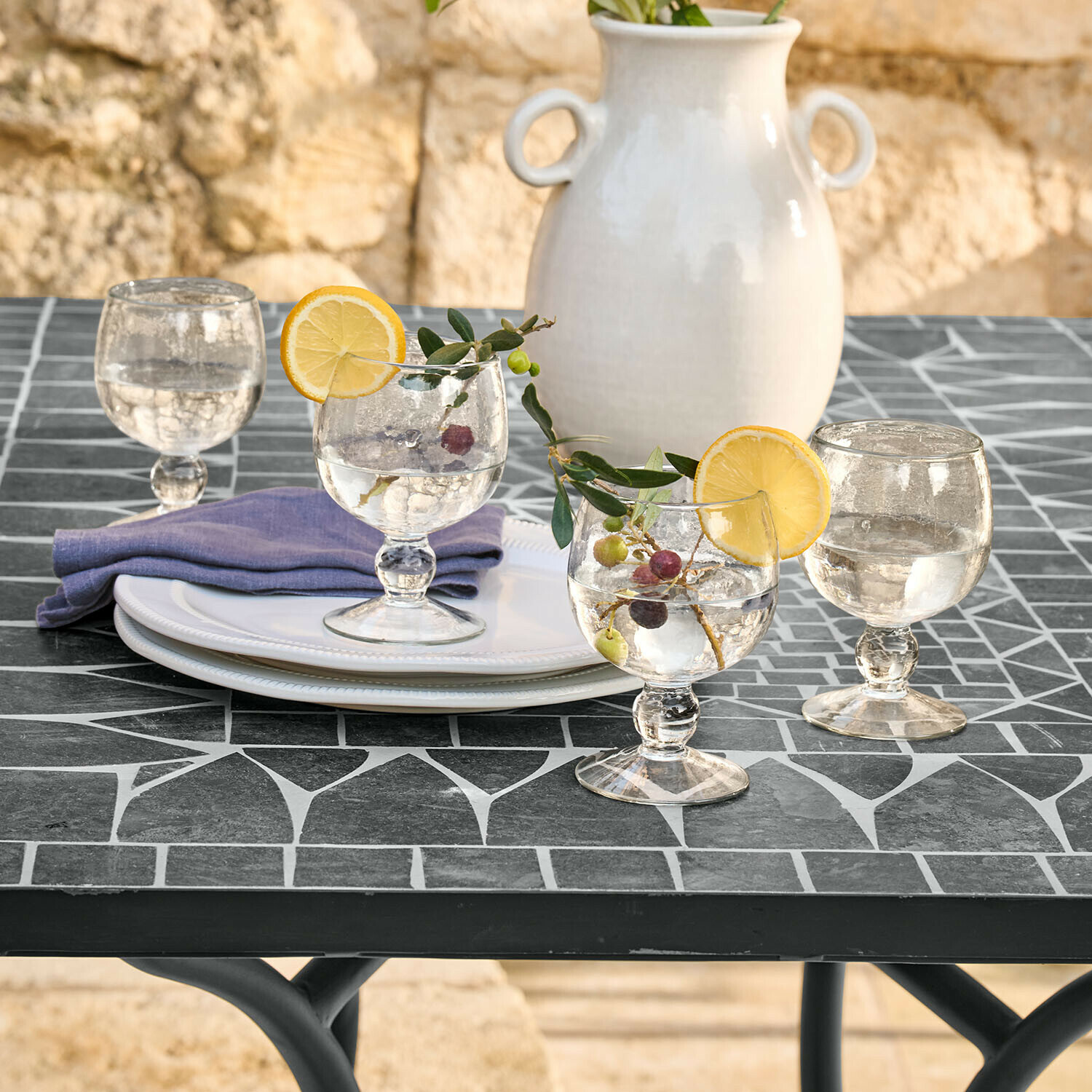 Glas 4er Set Vinoros Gläser mit Wasser und Zitronenscheiben auf schwarzem Mosaiktisch, weiße Keramikvase im Hintergrund
