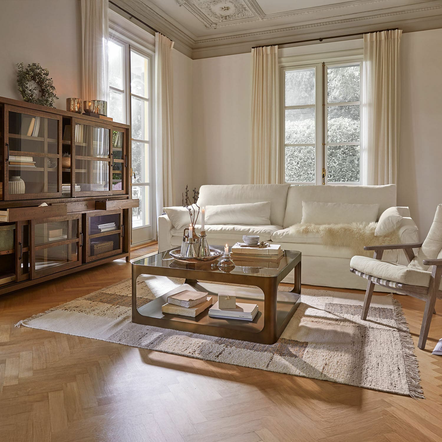 Gemütliches Wohnzimmer mit weißem Sofa, Holzvitrine und Metall-Couchtisch auf Teppich