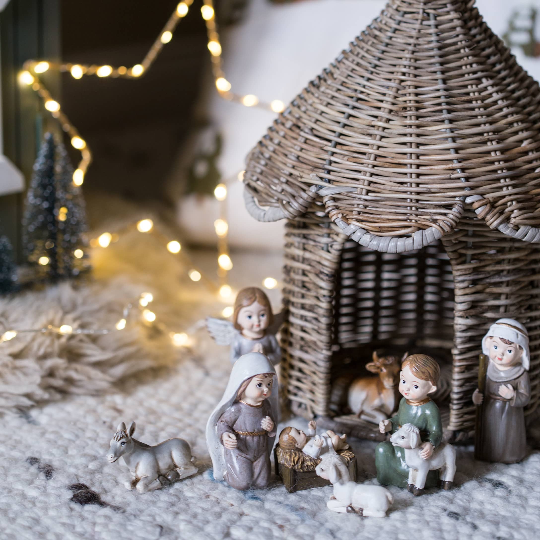 Weihnachtskrippenfiguren mit einem Korbhaus und Figuren auf einem weichen Teppich mit Lichterkette