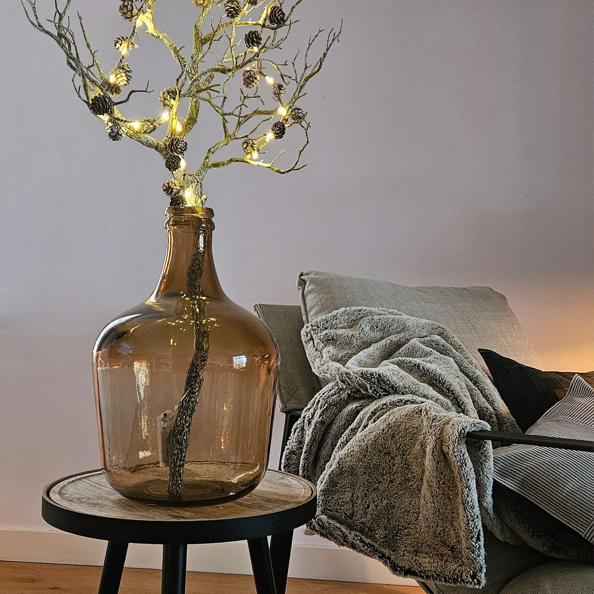 Braune Glasvase mit beleuchteten Zweigen auf Holzbeistelltisch im Wohnzimmer