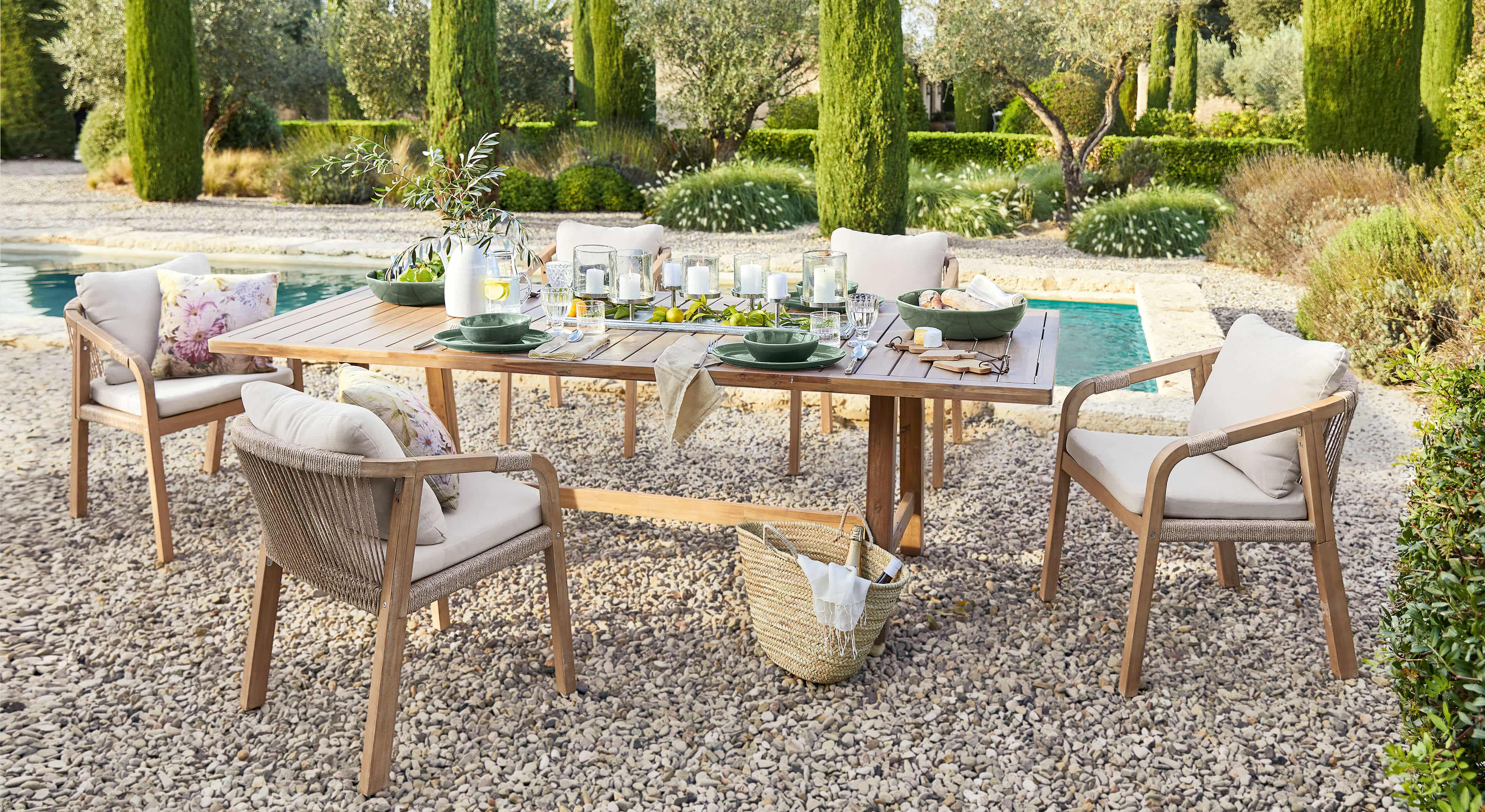 Gartenmöbel-Set mit Holztisch und beigen Stühlen auf Kieselstein-Terrasse neben Pool