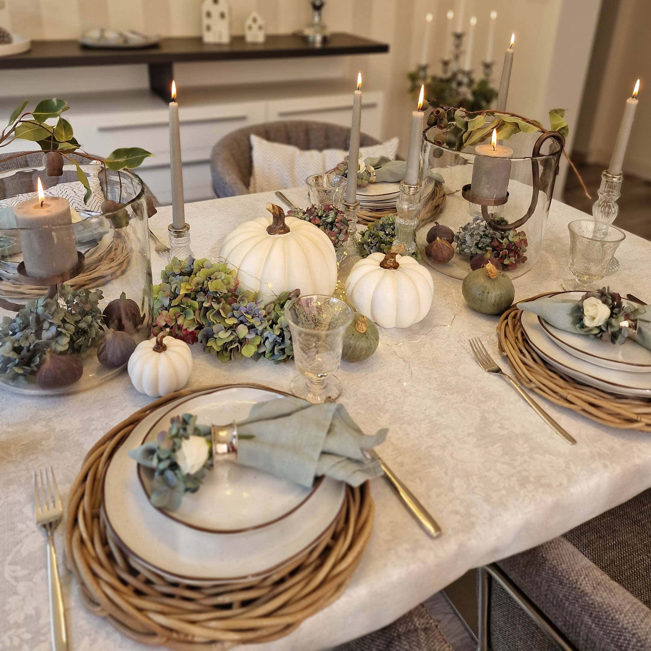 Elegante Herbsttischdeko mit weißen Kürbissen, Kerzen und natürlichen Akzenten auf Tischdecke