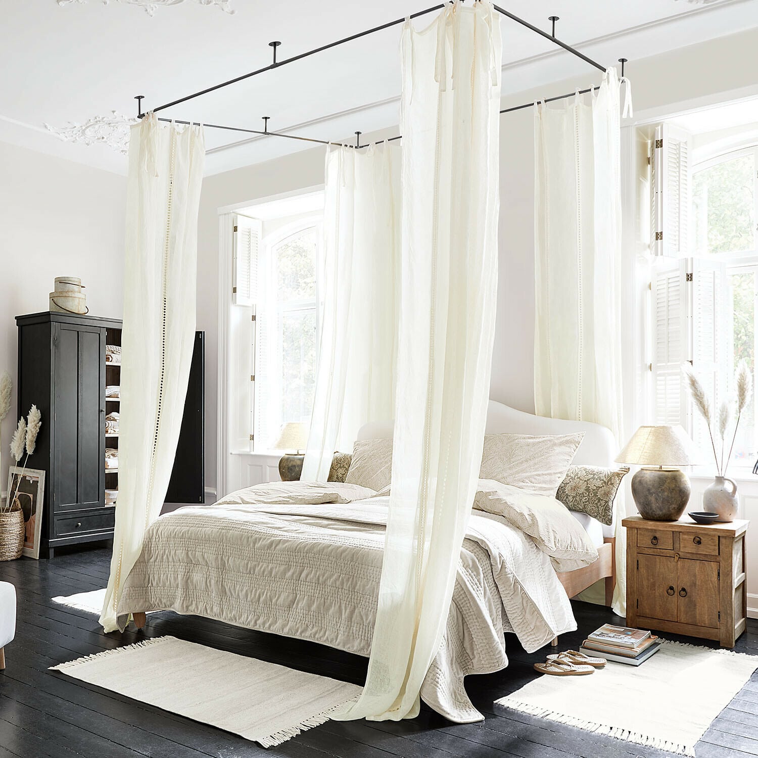 Gardine Elorine Schlafzimmer mit weißem Baumwoll-Baldachinbett und beiger Bettwäsche auf dunklem Holzboden, helles Tageslicht