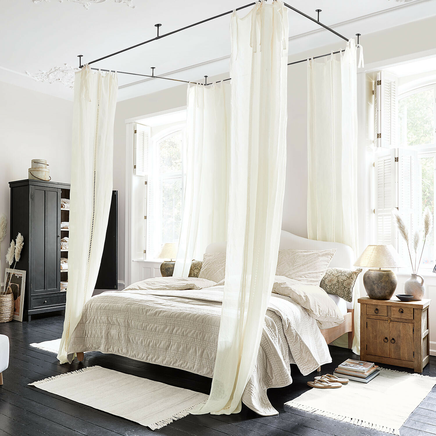 Gardine Elorine Schlafzimmer mit weißem Baumwoll-Baldachinbett und beiger Bettwäsche auf dunklem Holzboden, helles Tageslicht