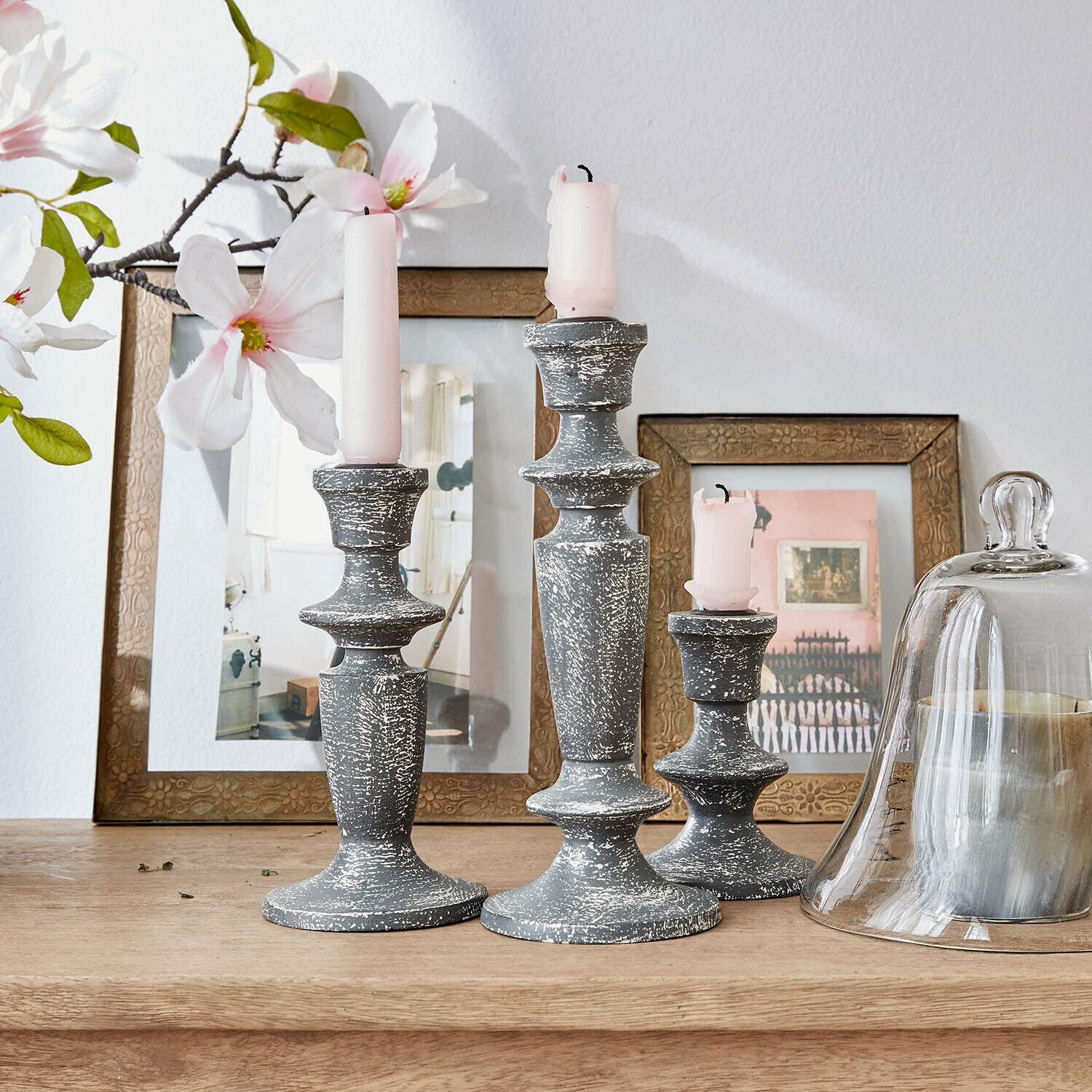 Drei graue Kerzenhalter aus antik wirkendem Holz mit rosa Kerzen auf Holztisch