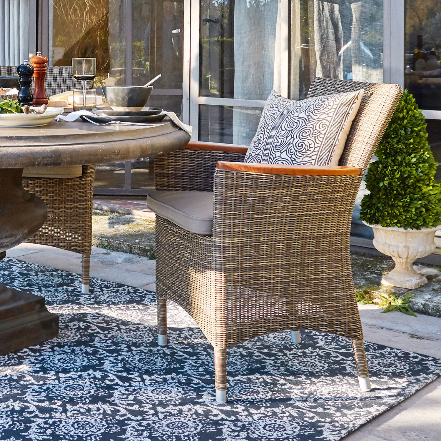 Sessel Casper Rattanstuhl in Naturfarbe mit Polster und Holzarmlehnen auf Terrasse neben Tisch