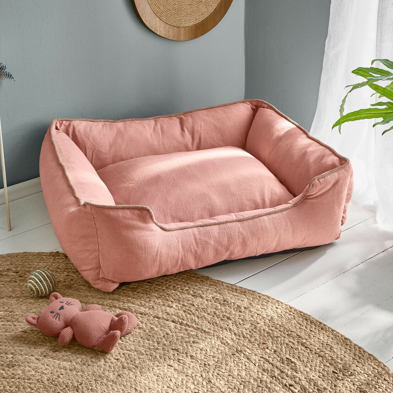 Rosa Hundebett aus weichem Stoff auf hellem Boden mit Katzenspielzeug und Ball