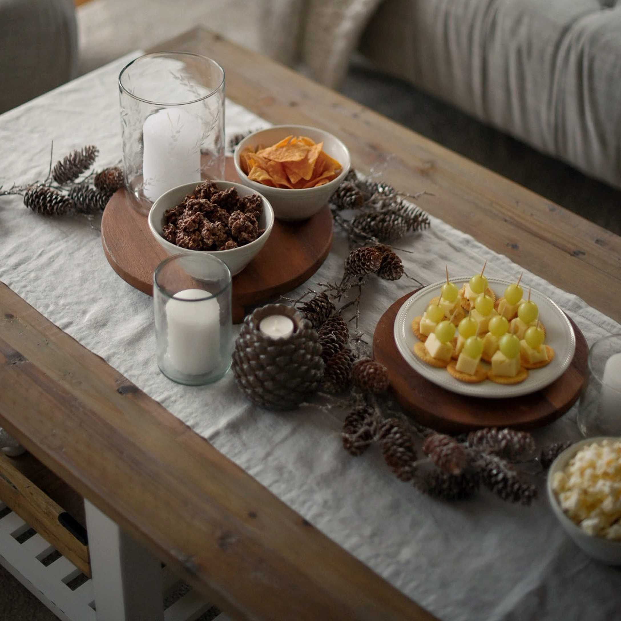 Holztablett mit Snacks und Kerzen auf Leinentischläufer mit Tannenzapfendekor