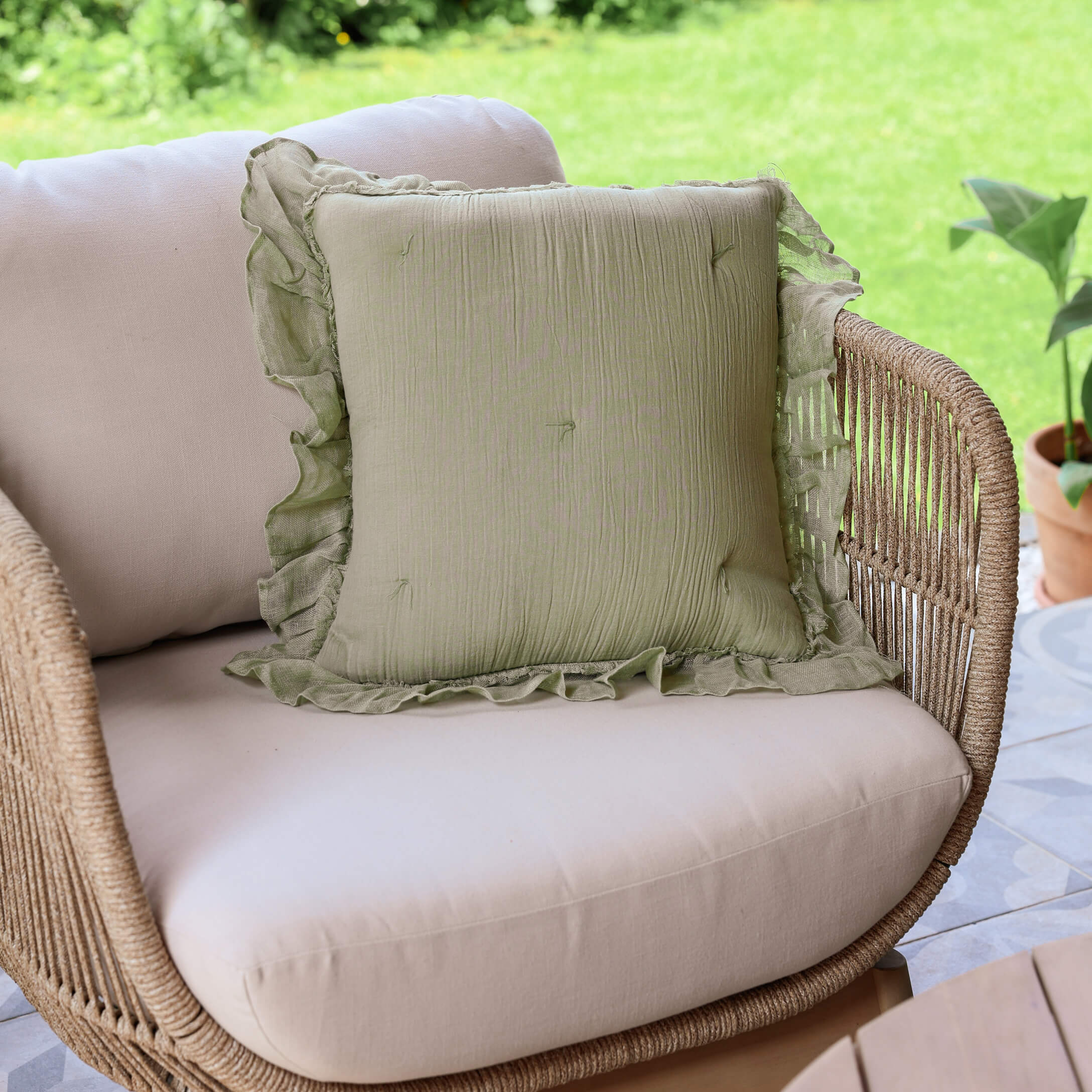 Grünes Leinen-Dekokissen mit Rüsche auf beigem Rattansofa auf der Terrasse